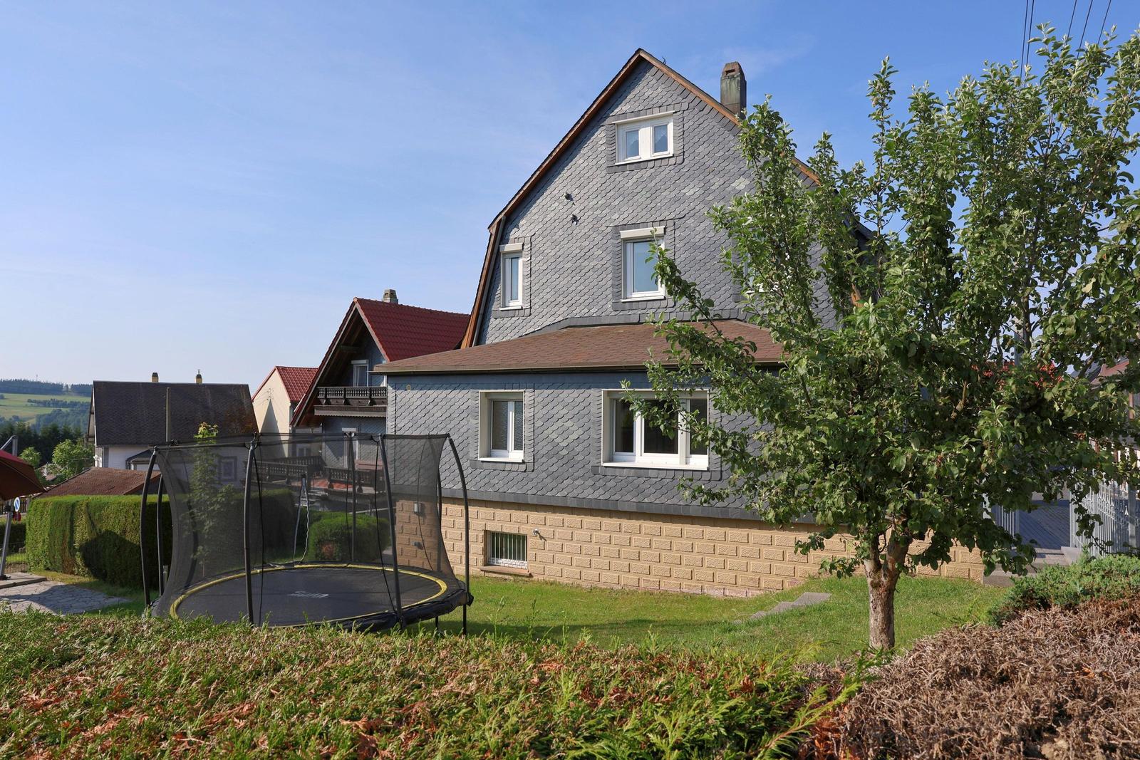 Haus mit Garten und Trampolin. Blick auf das Grundstück mit Baum und Rasen.