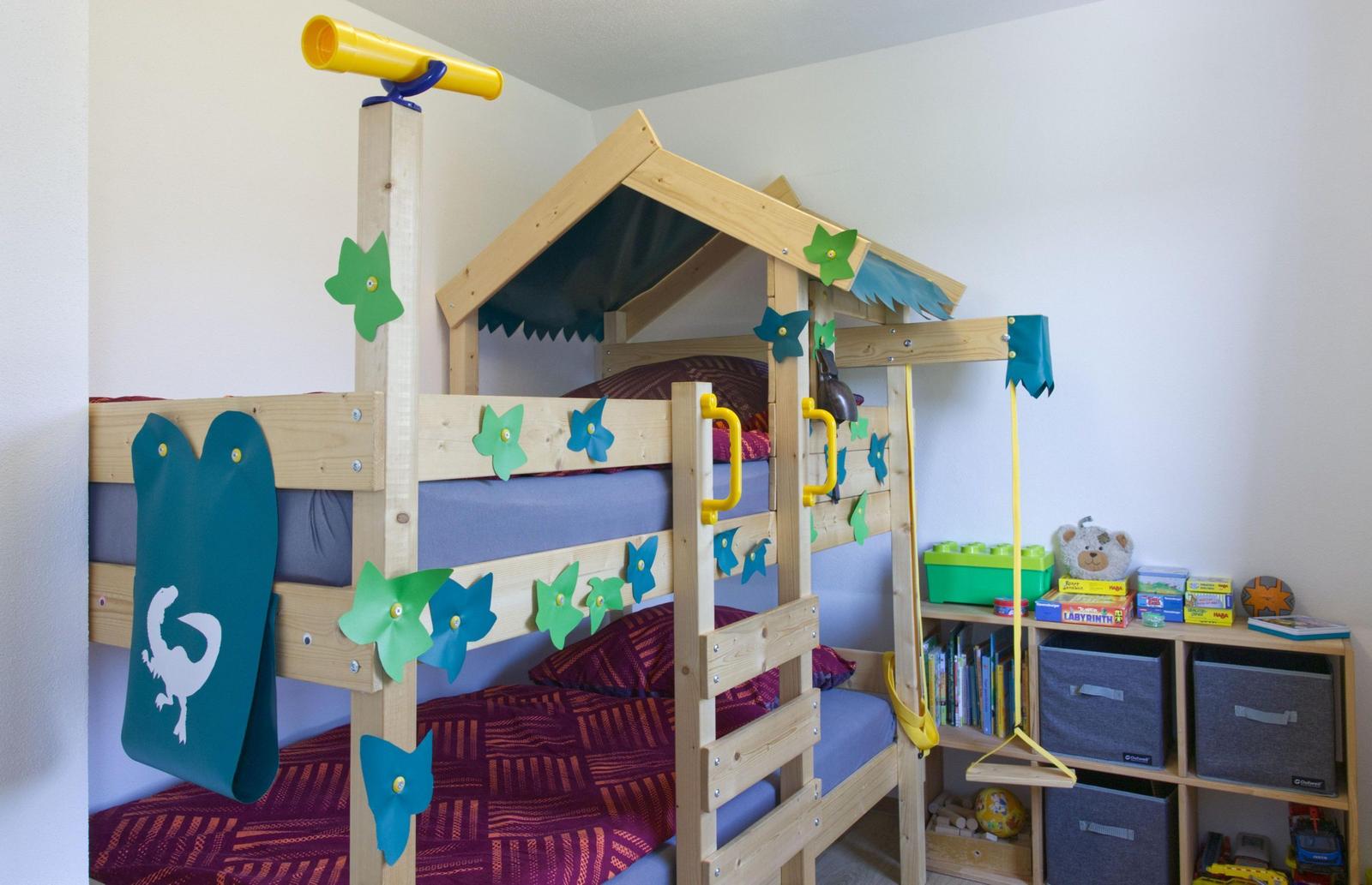 Ein Kinderzimmer mit einem hölzernen Doppelbett, Spielzeug und einem Regal mit Büchern und Kisten.