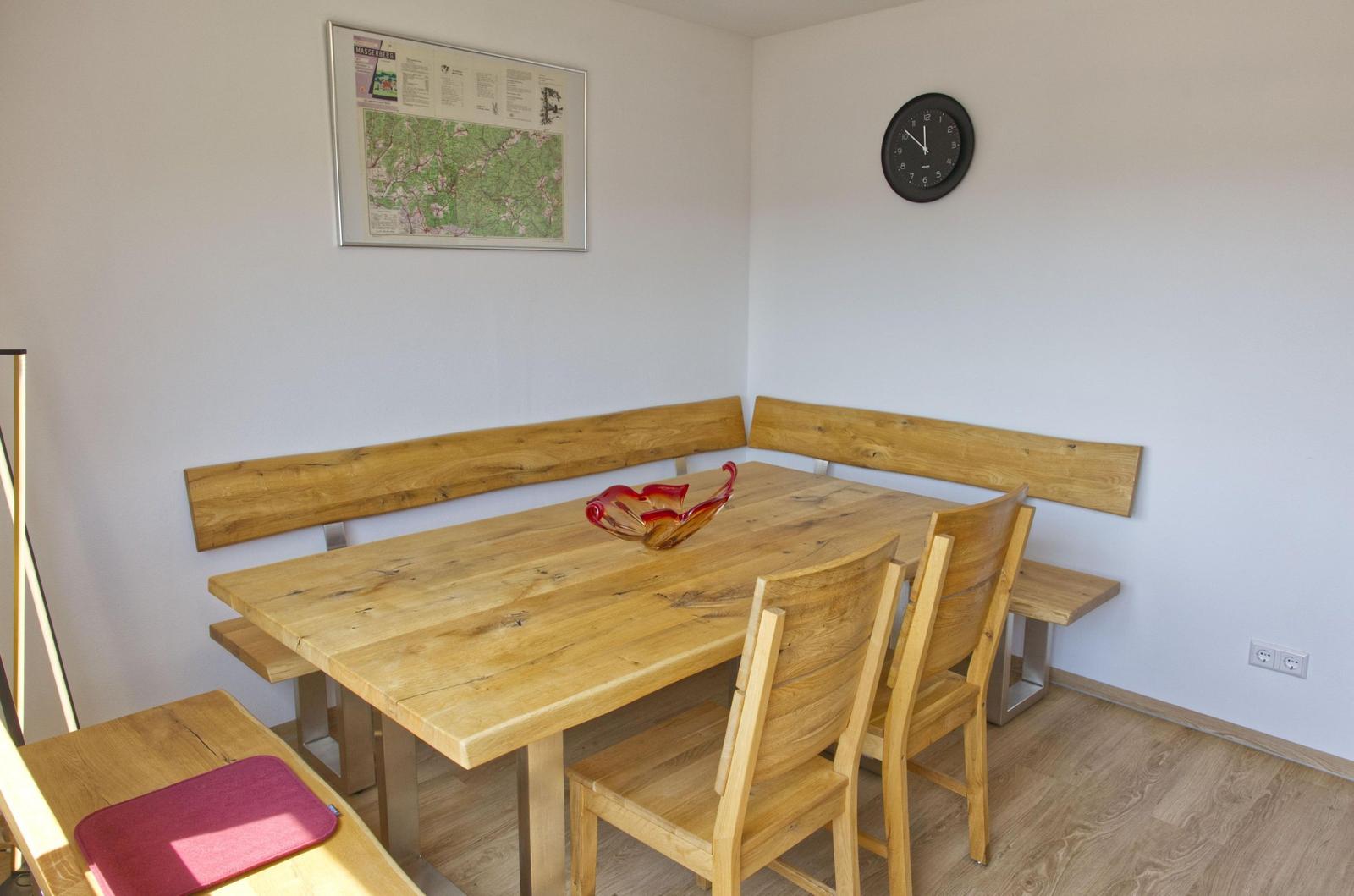 Esszimmer mit Holztisch, Bänken und Stühlen. Wanduhr und Karte an der Wand.