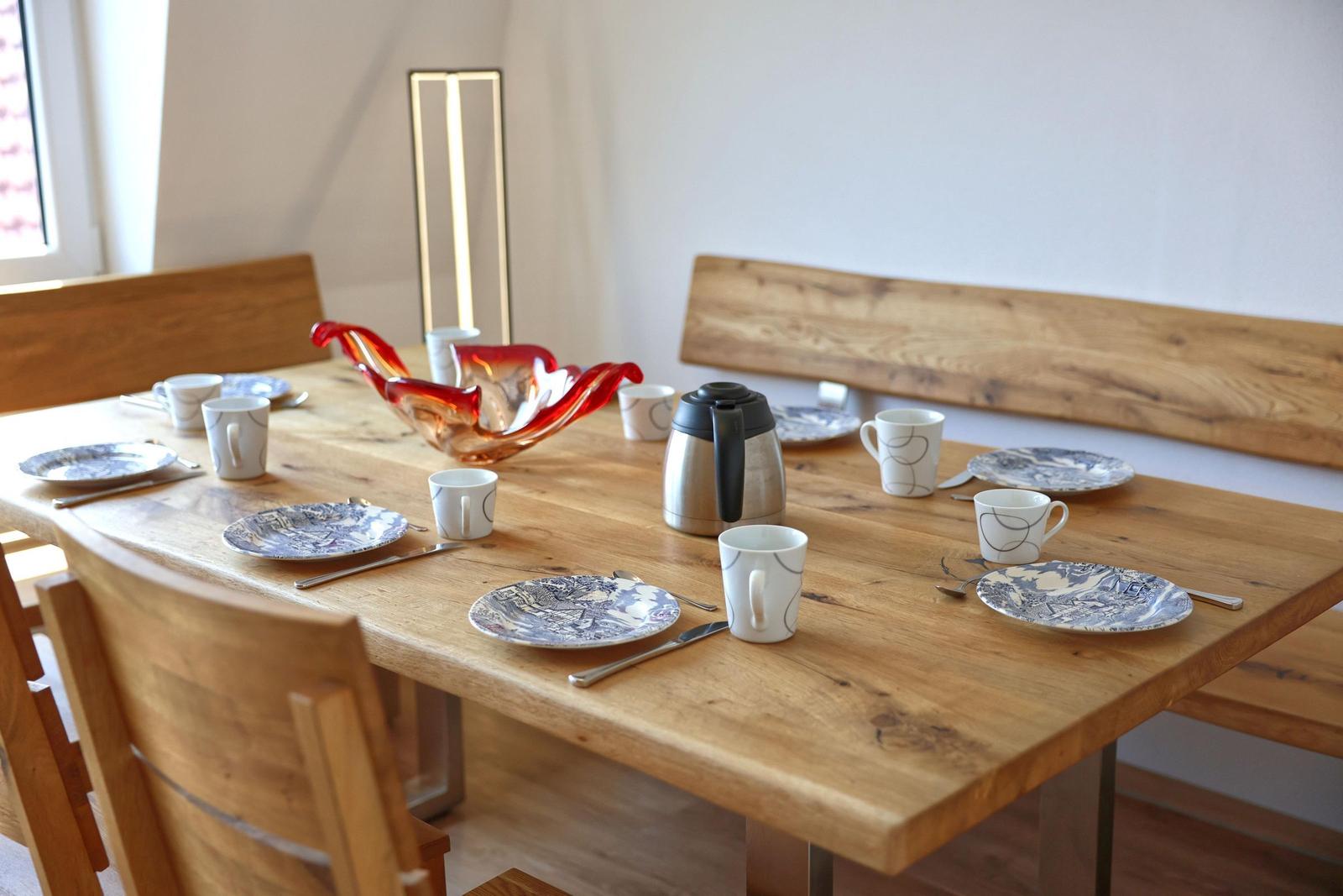 Holztisch mit Platz für sechs Personen, Geschirr und Kaffeekanne