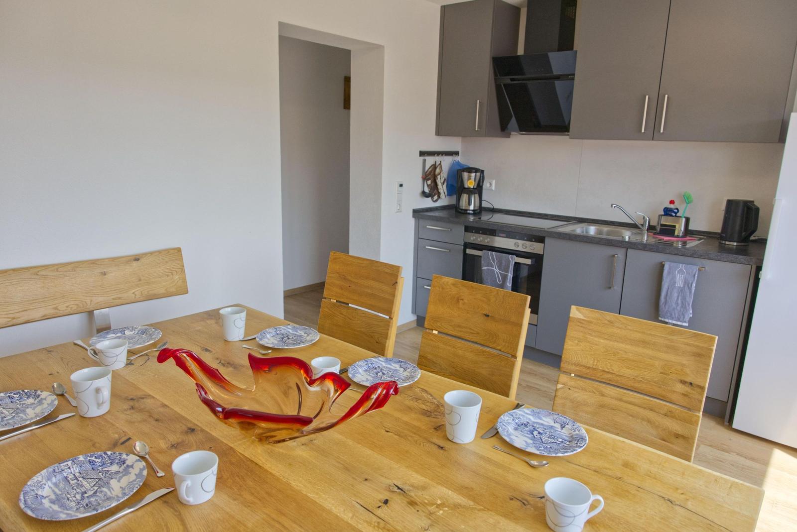 Essbereich mit Holztisch und Stühlen. Küche mit grauen Schränken und Edelstahlgeräten.