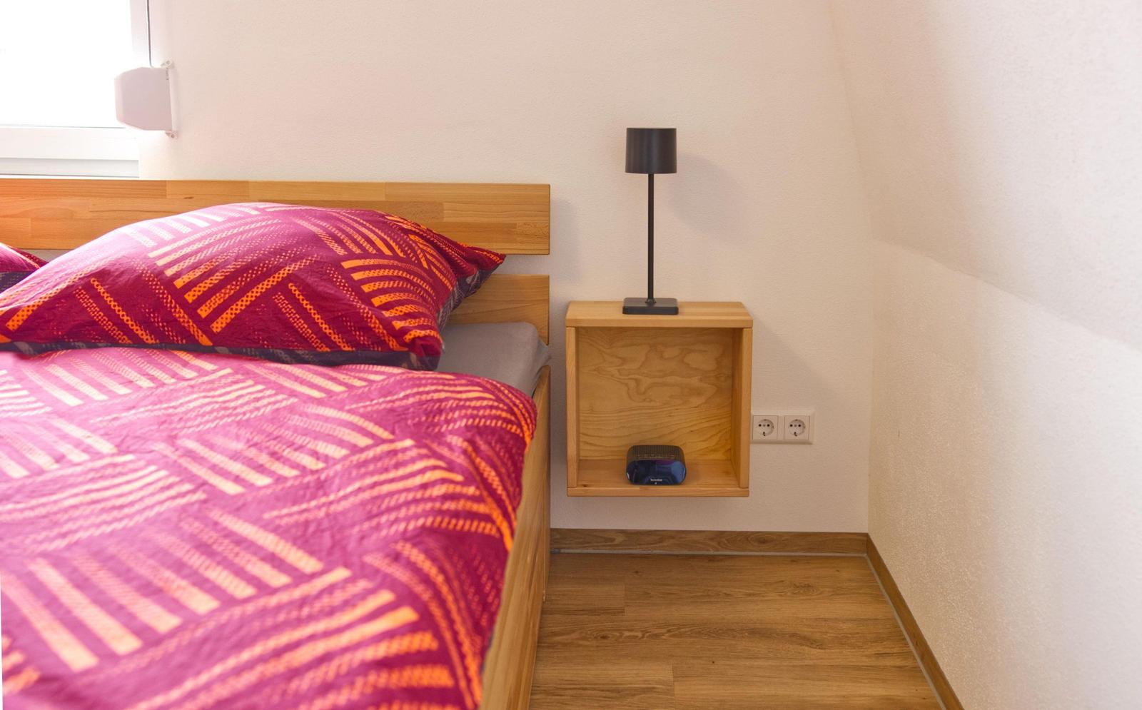 Schlafzimmer mit Bett, Nachttisch und Lampe. Holzfußboden und Wandbeleuchtung.