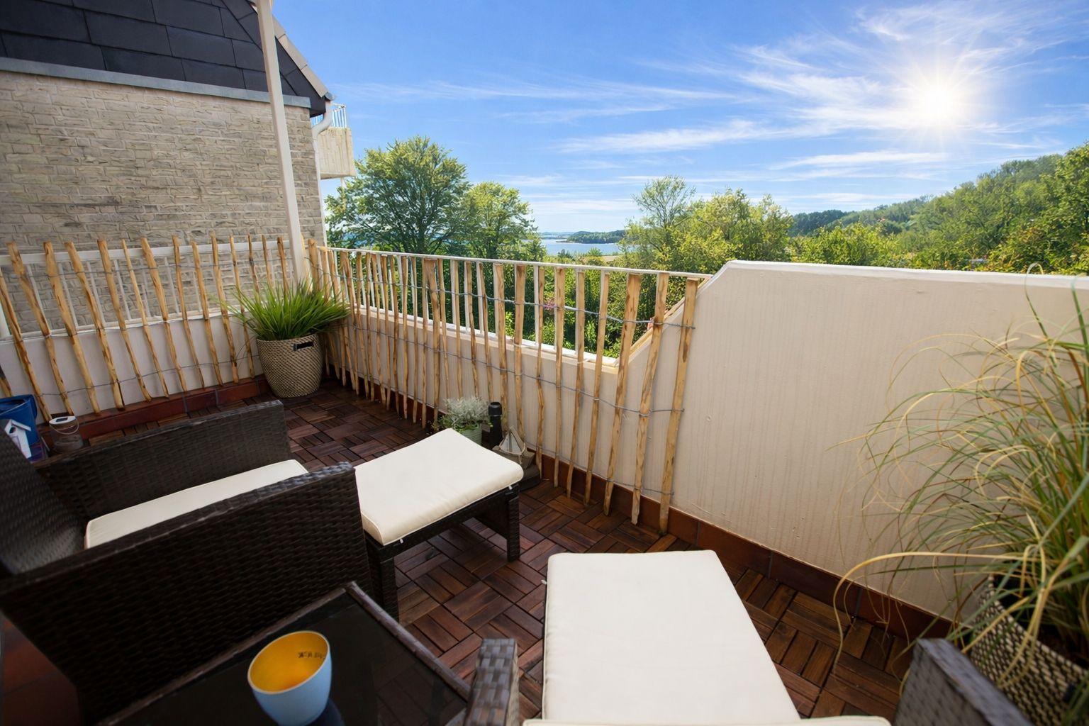 Terrasse mit Sitzgelegenheiten und Blick auf Wald und Wasser.