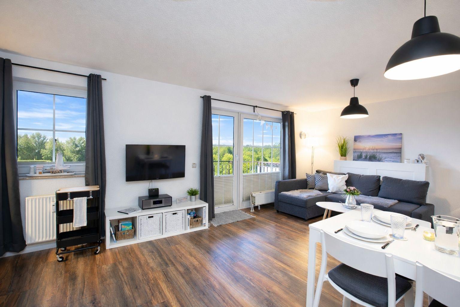 Wohnzimmer mit Essbereich, TV, Balkon und Holzboden.