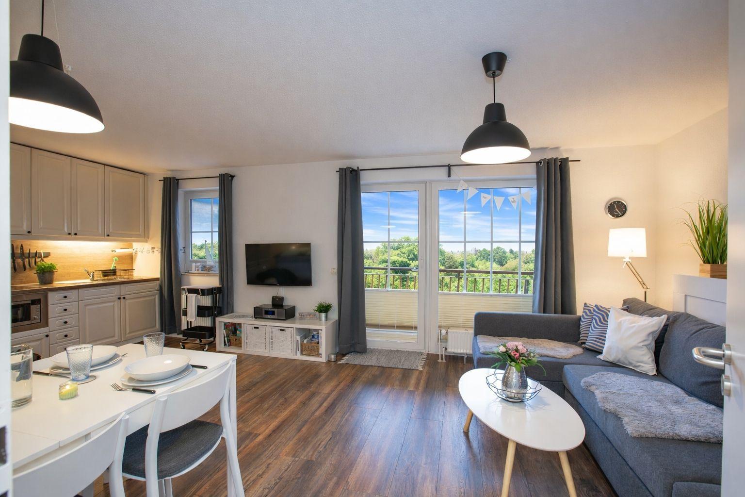 Wohn- und Essbereich mit Küche, Sofa und Balkon mit Blick auf Grünflächen.