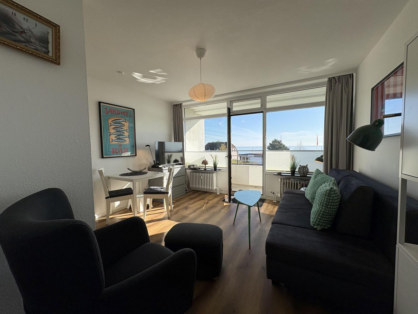Wohnzimmer mit Sofa, Sessel und Blick auf Balkon mit Meerblick.