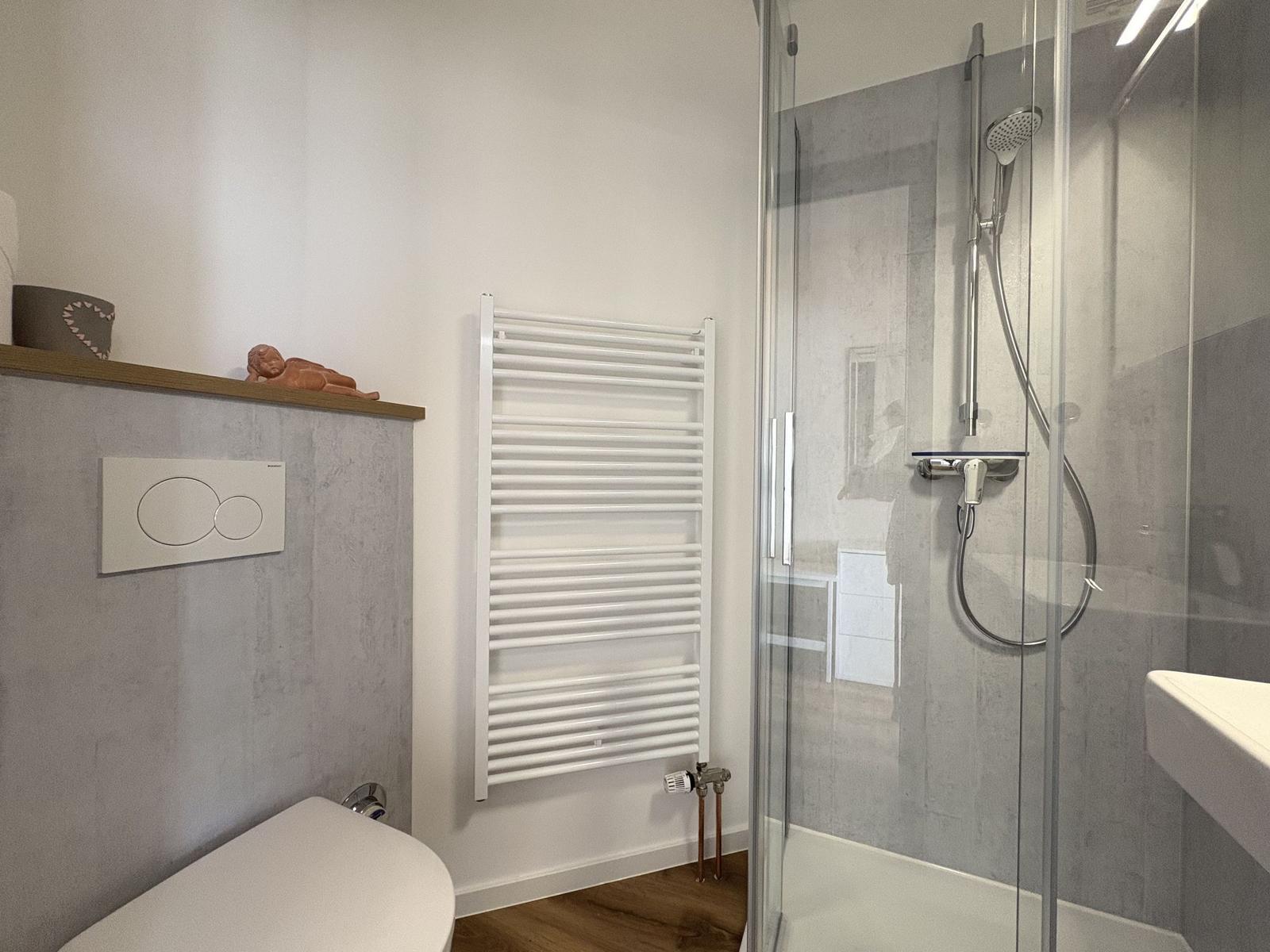 Bad mit Dusche, Toilette und Heizkörper an der Wand.