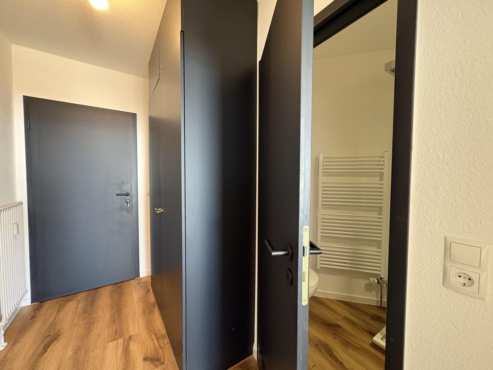 Flur mit Tür, Schrank und Blick in Bad mit Heizung.