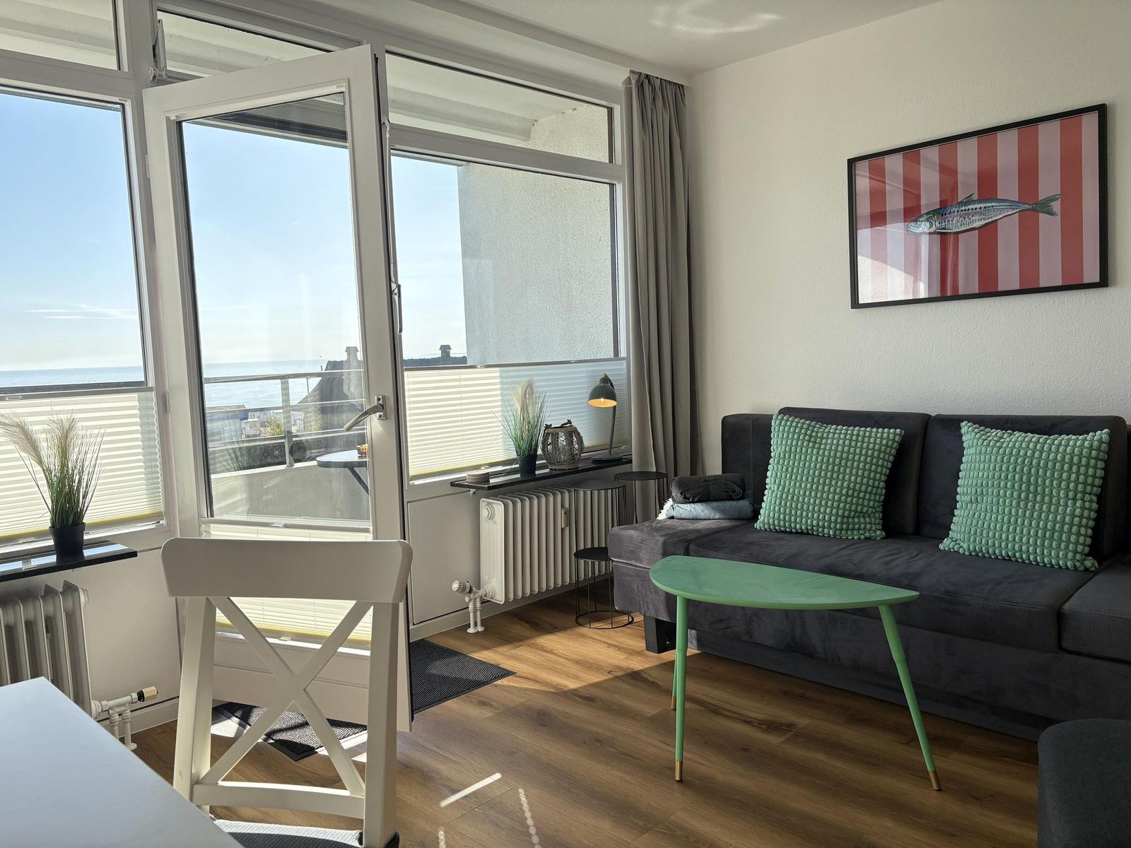Wohnzimmer mit Sofa, Tisch und Blick aufs Meer durch Balkontür.
