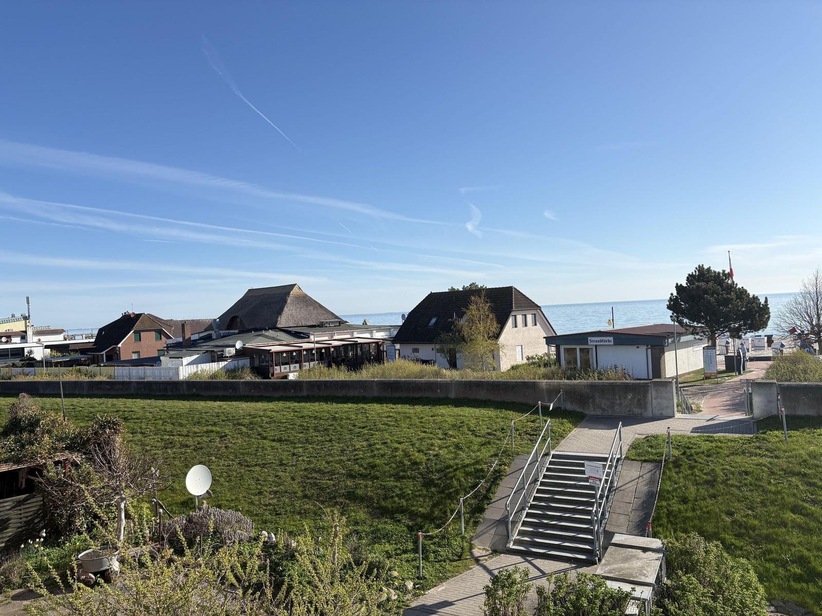 Grüner Hang mit Steigweg zum Strand. Im Hintergrund Häuser und Meer.