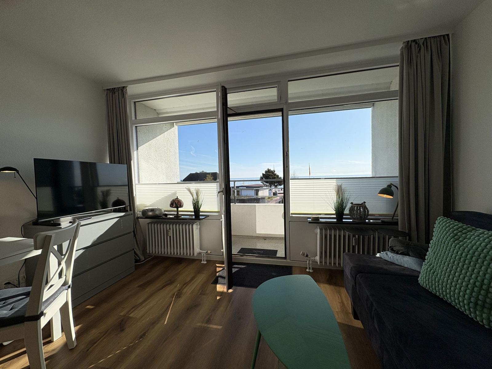 Wohnzimmer mit Sofa, Fernseher und Balkon mit Meerblick.