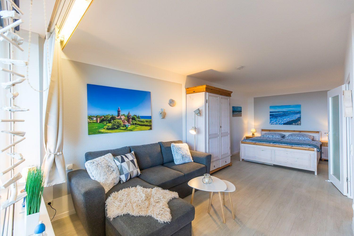 Wohn- und Schlafzimmer mit Sofa, Bett und Wandbildern.