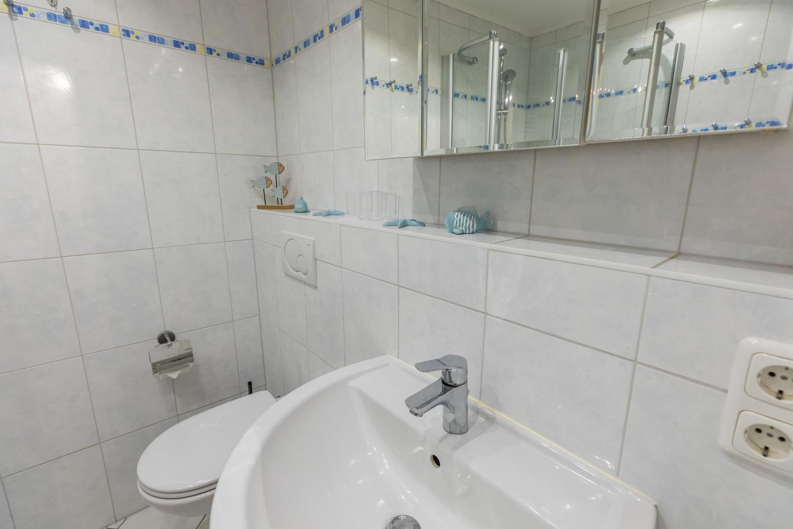 Badezimmer mit Waschbecken, Spiegel und Toilette. Wandfliesen und blaue Dekoration.