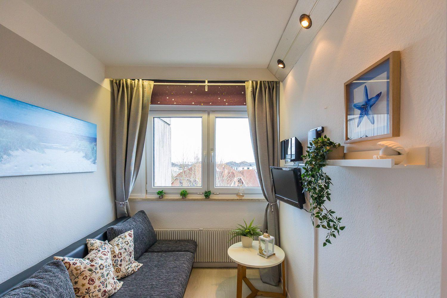 Ein Wohnzimmer mit Sofa, Fenster, Wandbild und TV. An der Wand hängt ein Bild mit einer Seestern.