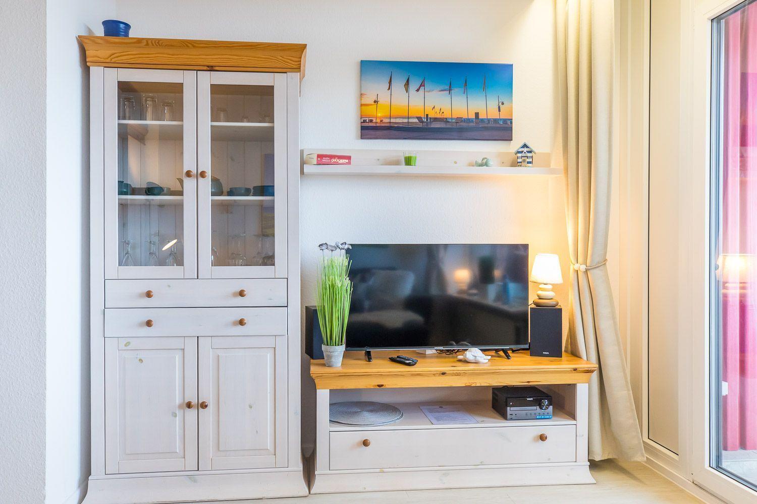 Ein Wohnzimmer mit Fernseher, Schrank und Wandbild.
