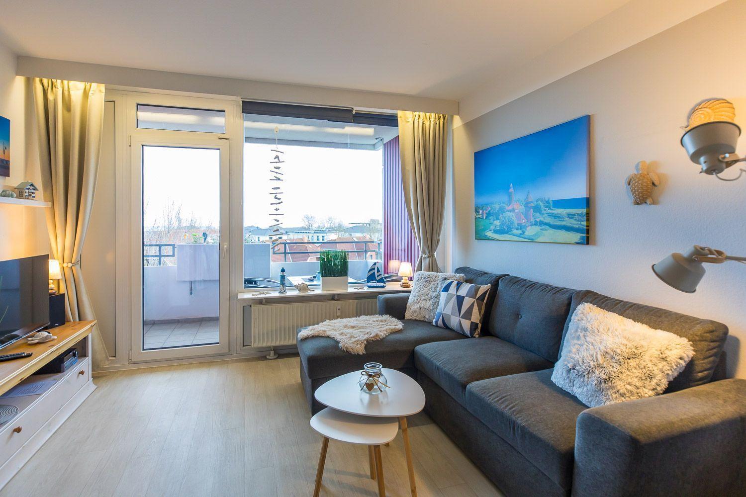 Wohnzimmer mit Sofa, Couchtisch und Balkonansicht. Wandbild und Stehlampe sichtbar.