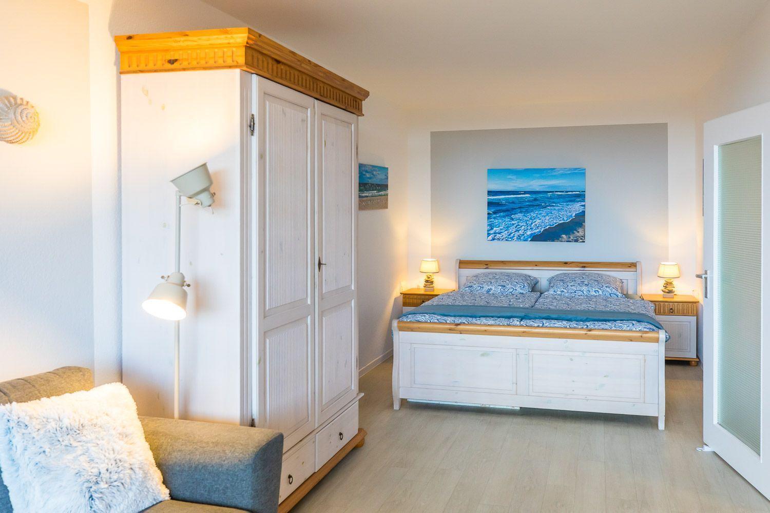 Schlafzimmer mit Bett, Kleiderschrank und Wandbild mit Meeresmotiv.