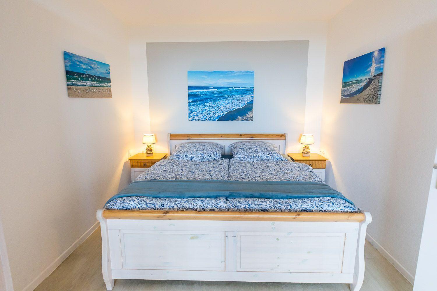 Schlafzimmer mit Doppelbett, zwei Nachttischen und Wandbildern mit Meeresmotiven.