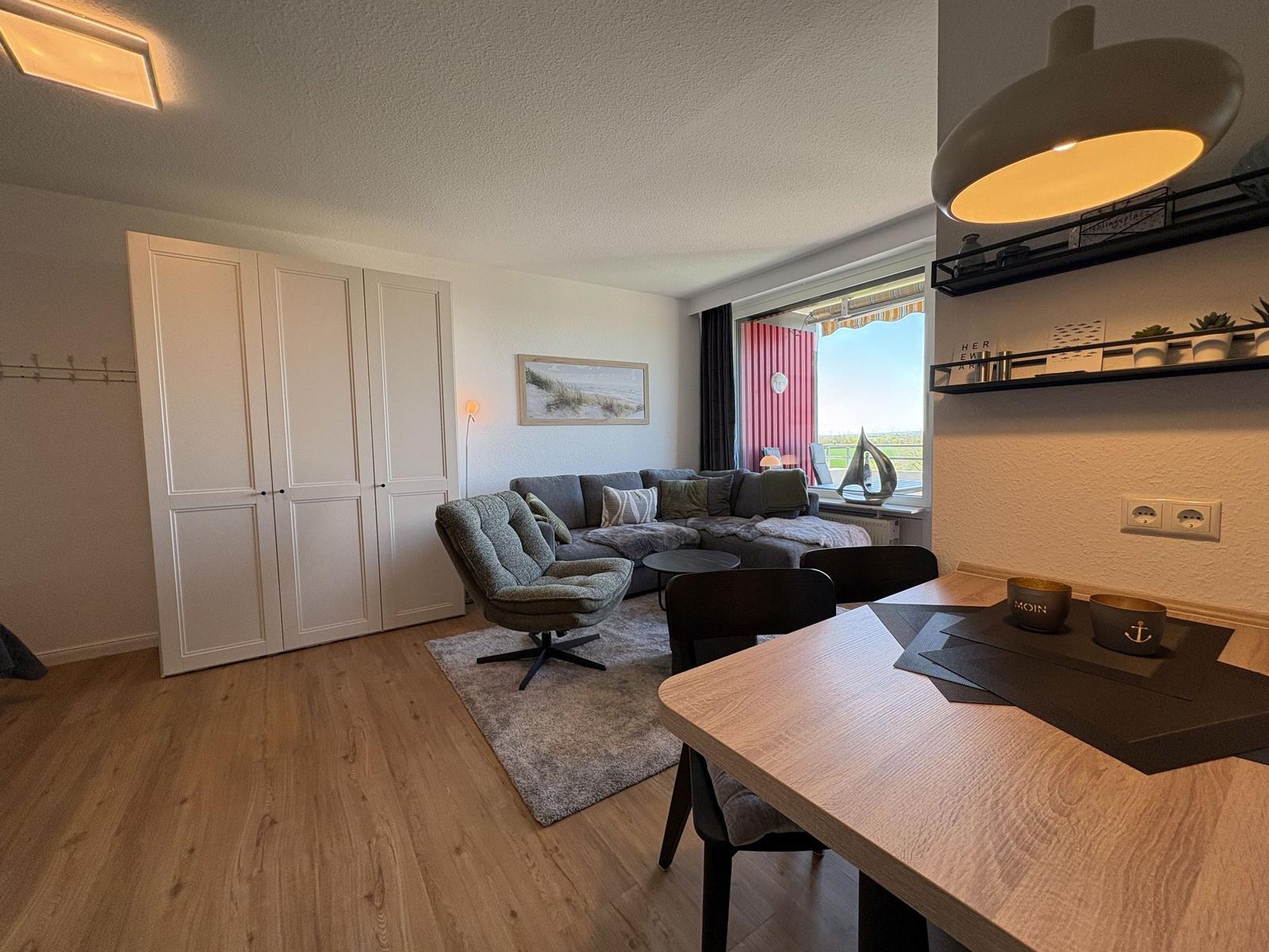 Wohn- und Essbereich mit Sofa, Stuhl und Tisch. Fenster mit Blick auf Außenbereich.