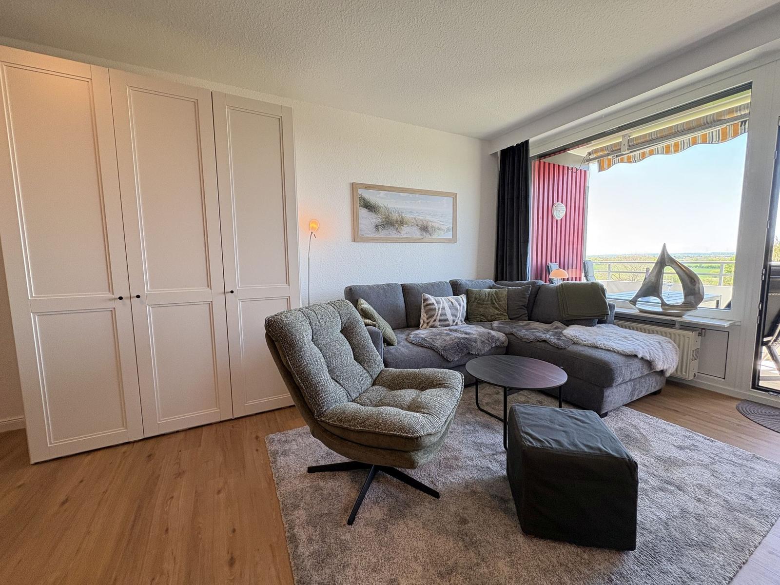 Wohnzimmer mit Sofa, Sessel und Balkonansicht