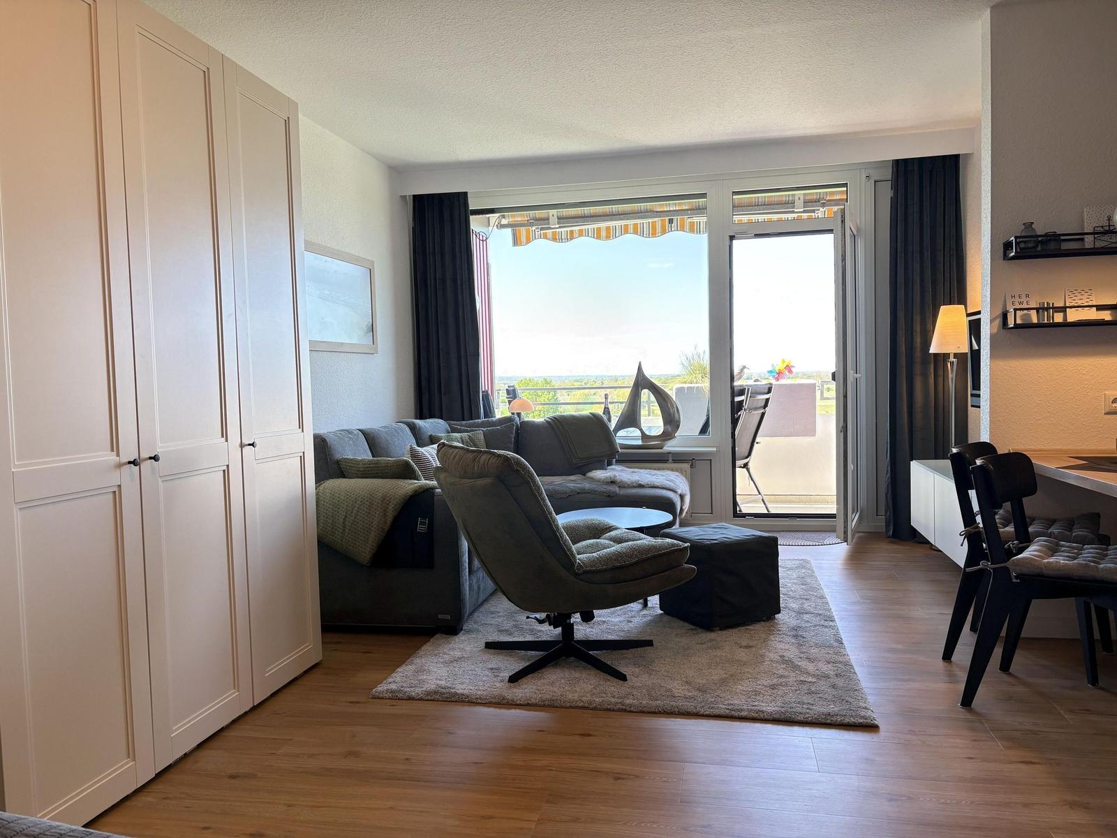 Wohnzimmer mit Sofa, Sessel und Balkon. Holzboden und weiße Schränke.
