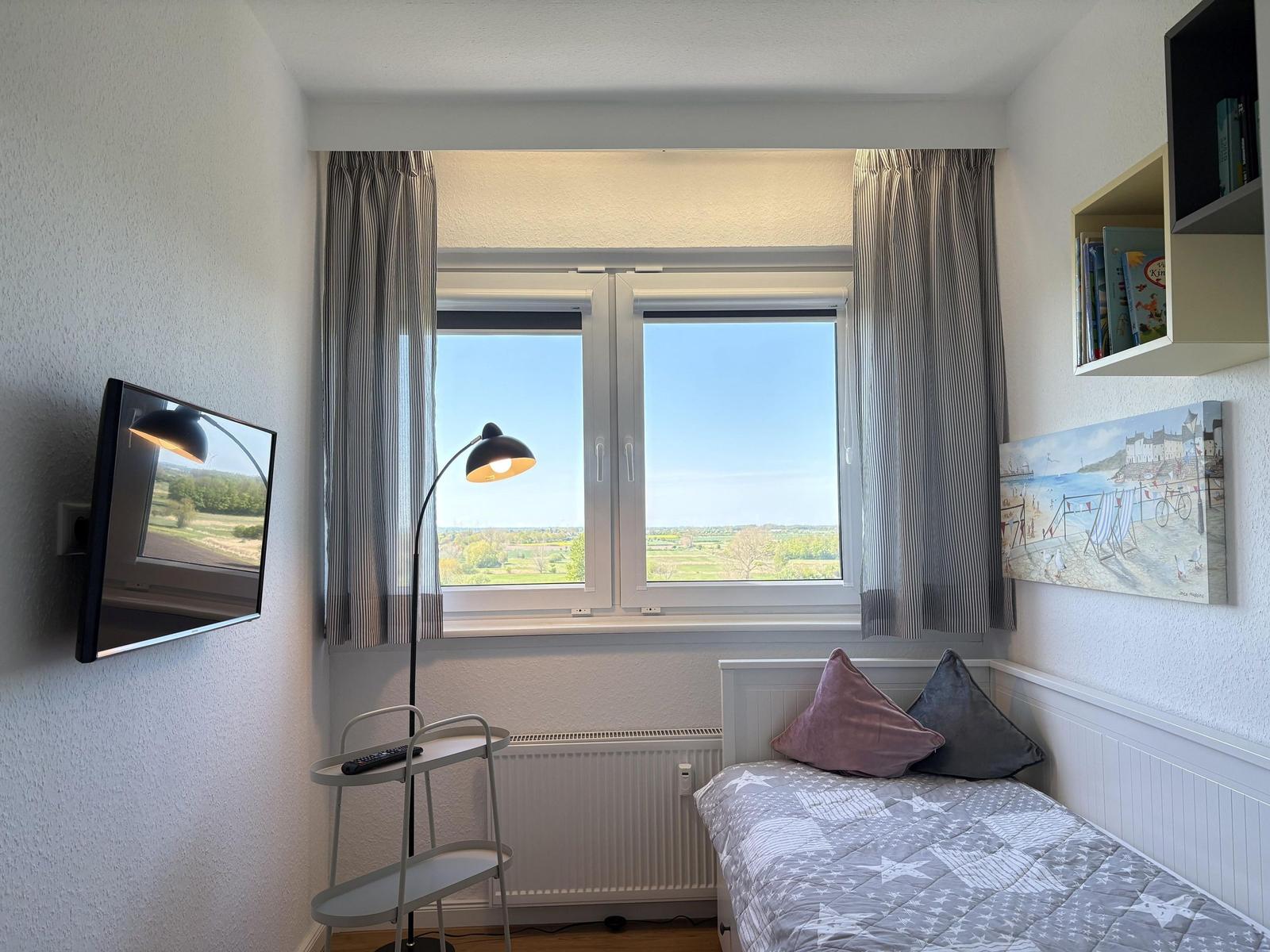 Zimmer mit Bett, Fenster und Wandbild. Fernseher an der Wand.
