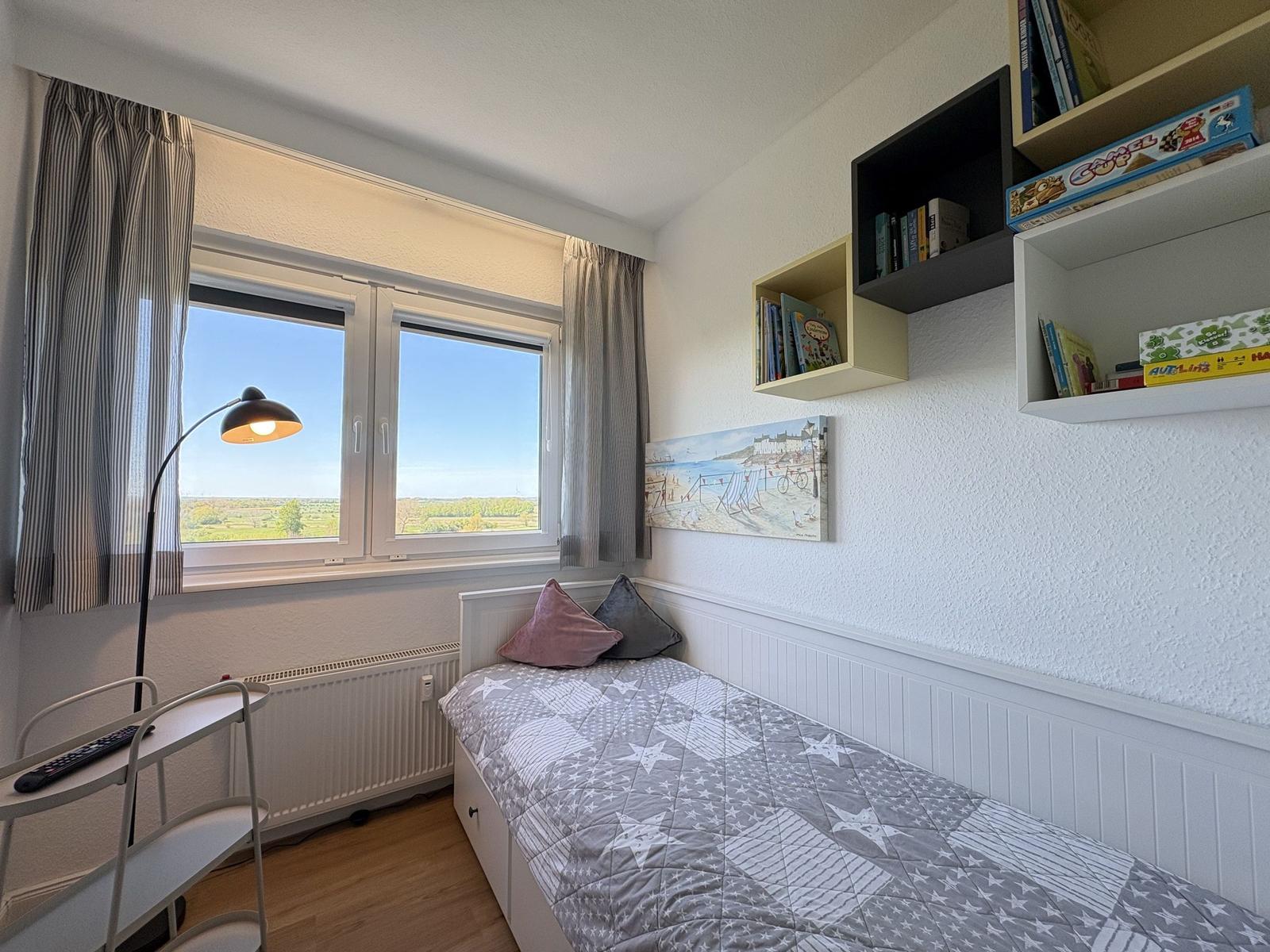 Schlafzimmer mit Bett, Fenster und Regalen an der Wand.