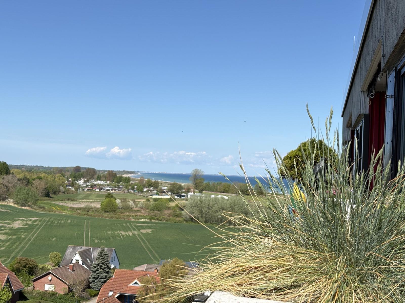 Blick auf Felder, Häuser und Meer unter blauem Himmel
