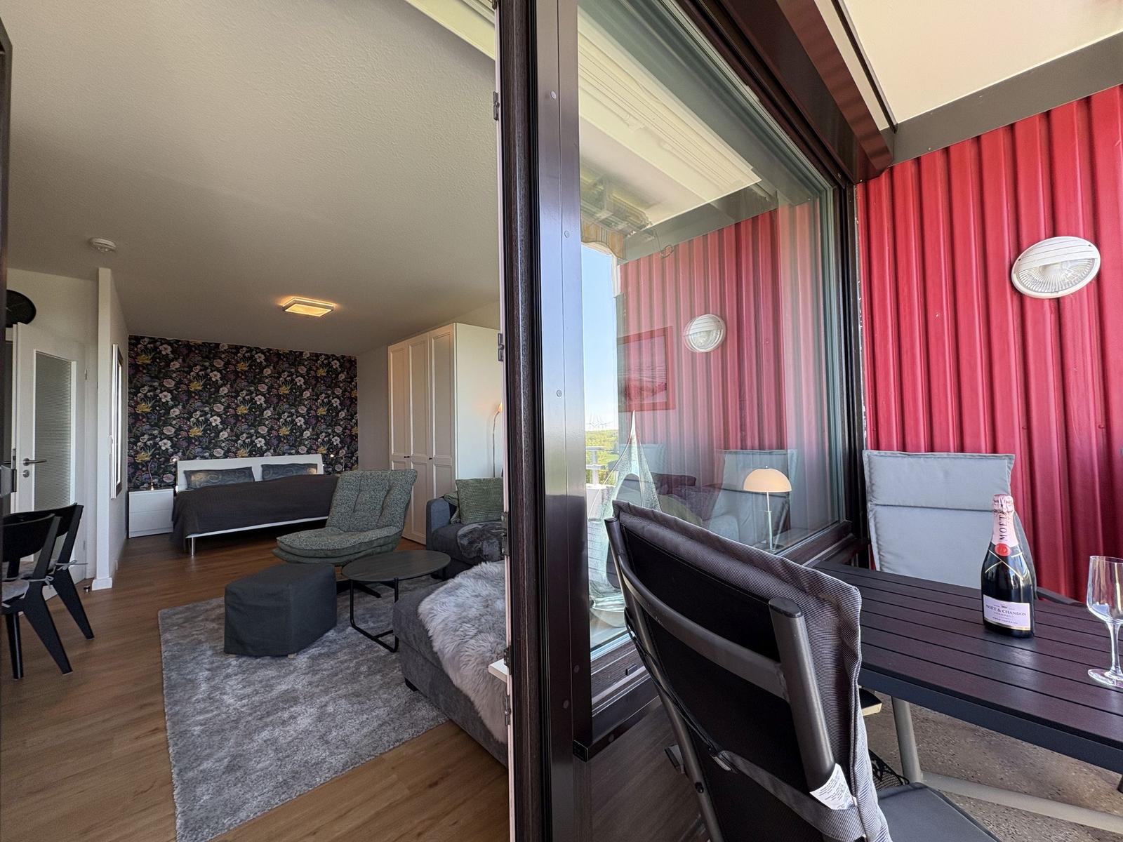 Terrasse mit Tisch und Stühlen. Im Hintergrund Wohnzimmer mit Bett und Sitzgelegenheiten.