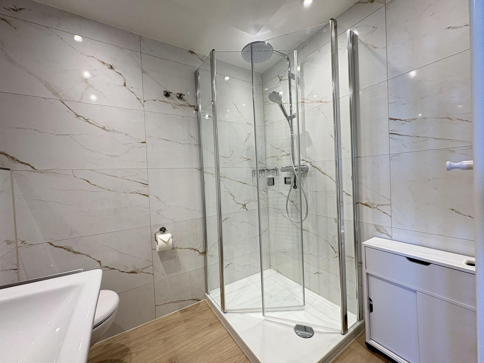 Badezimmer mit Dusche, Toilette und Waschtisch. Wände aus Marmorfliesen.