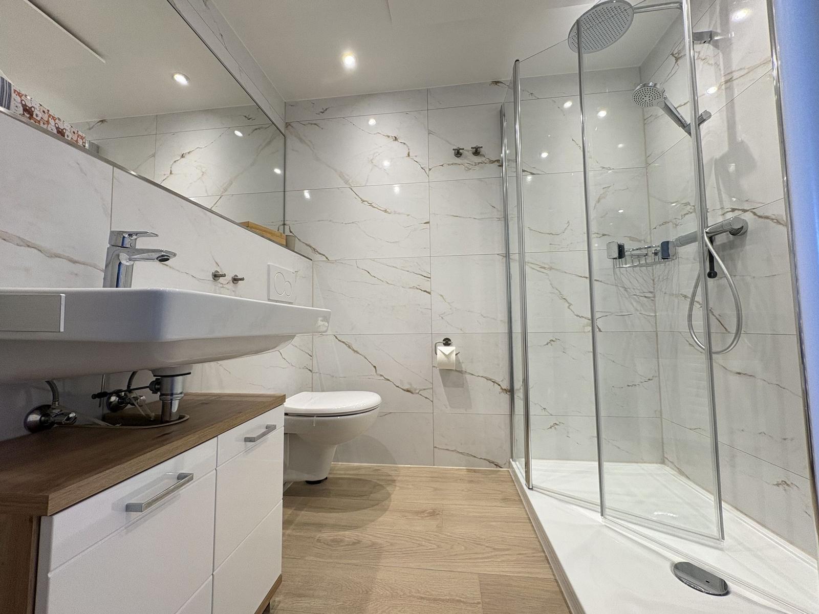 Badezimmer mit Dusche, Waschbecken und Toilette. Fliesen und Holzboden.