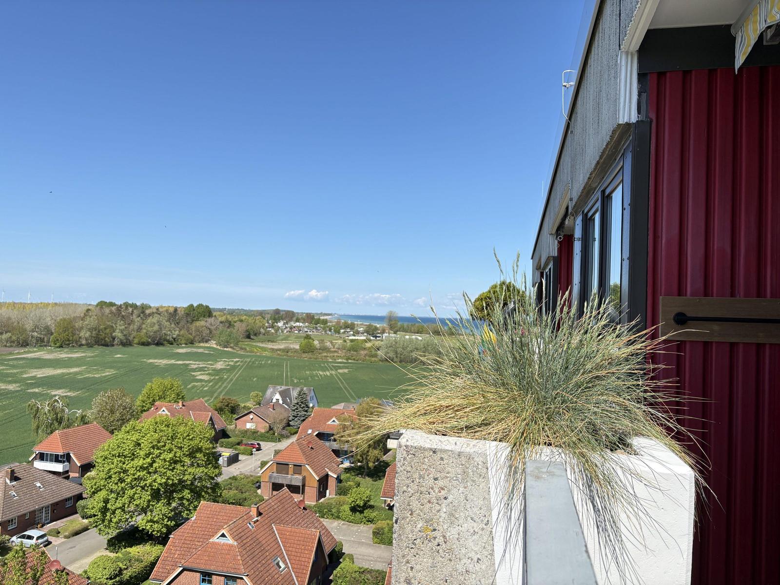 Blick von Balkon auf Felder, Häuser und Meer unter blauem Himmel.
