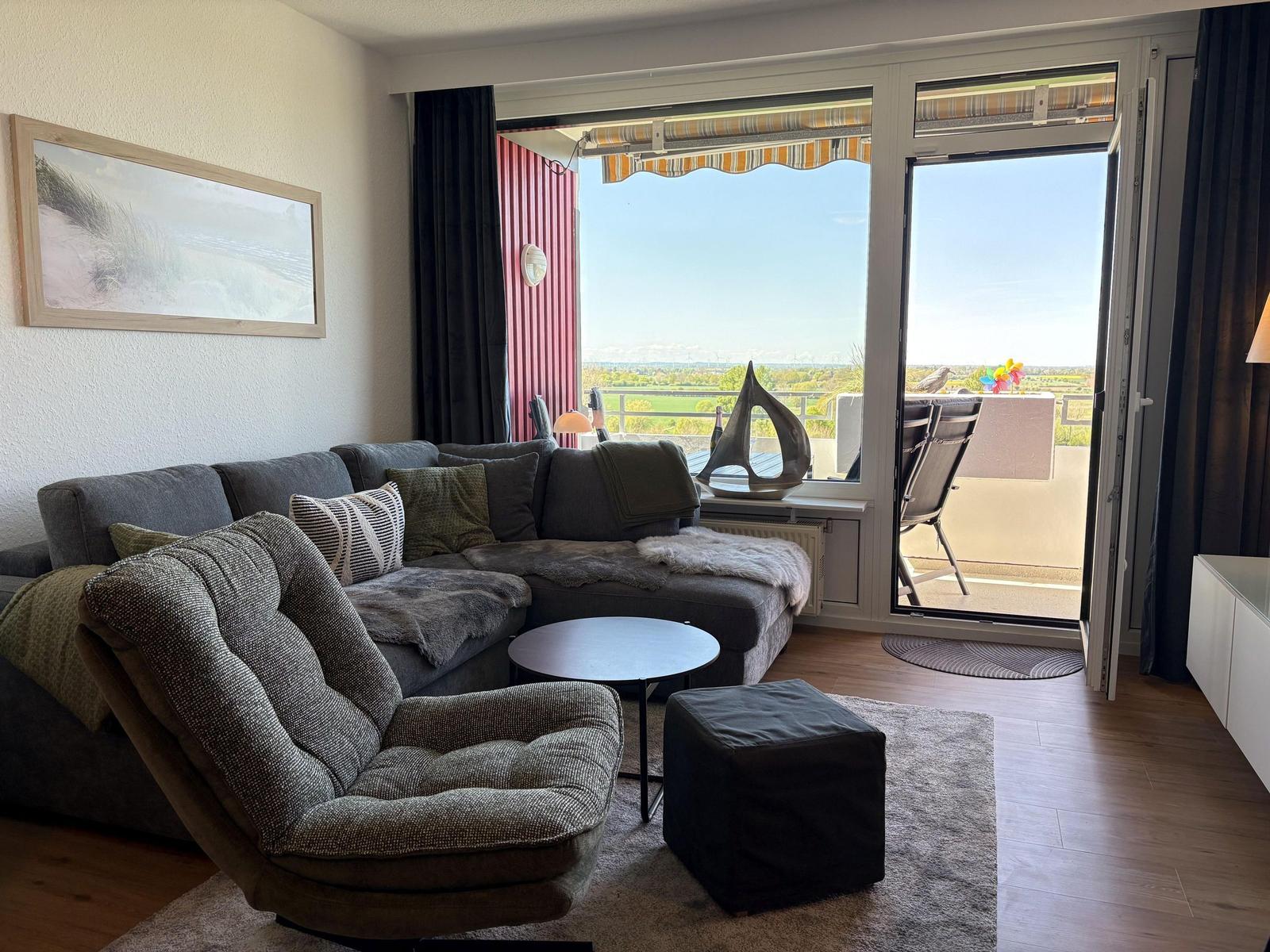 Wohnzimmer mit Sofa, Sessel und Balkonblick auf Landschaft