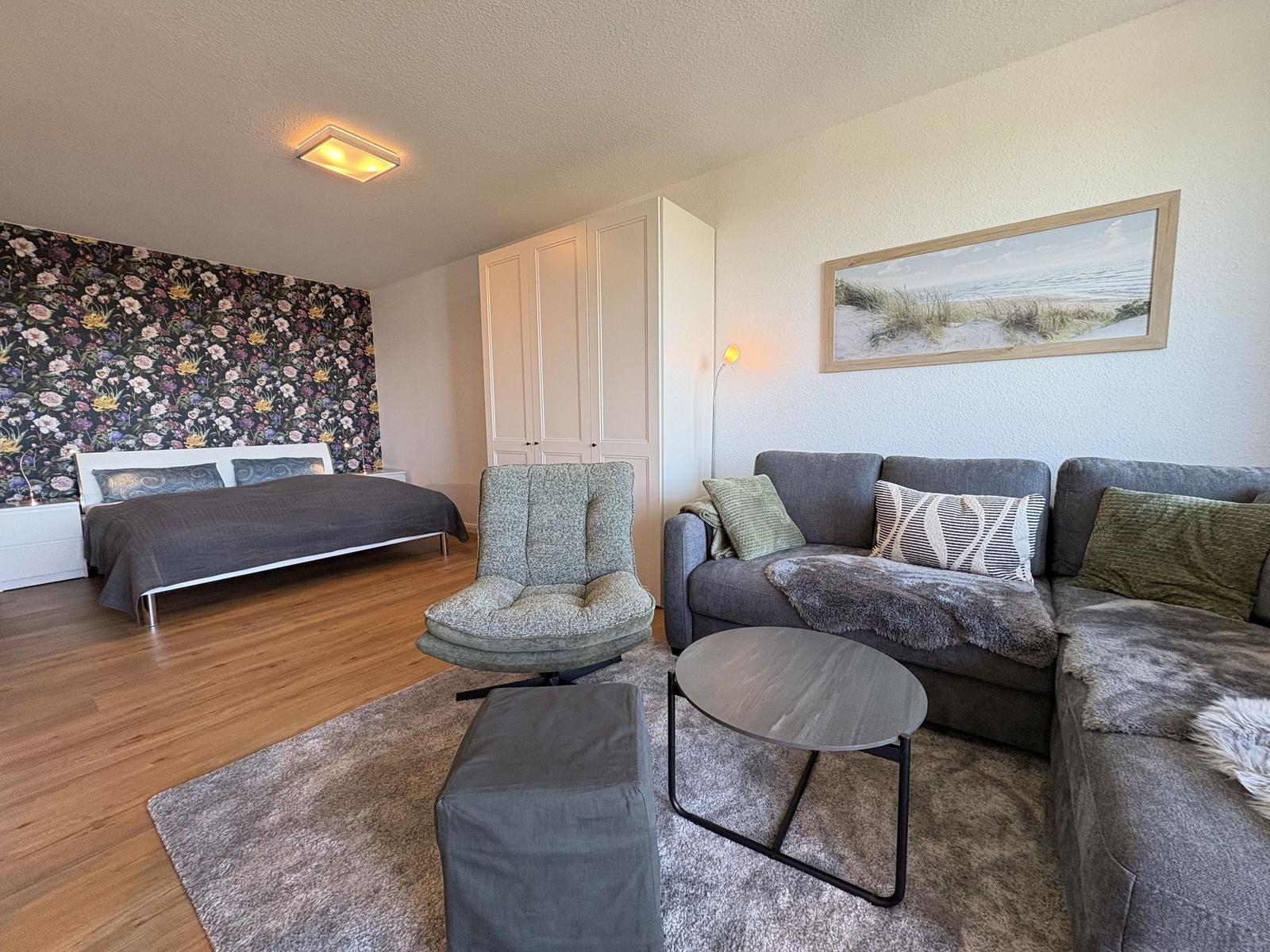 Schlafzimmer mit Bett und floraler Wand. Wohnbereich mit Sofa und Sessel.