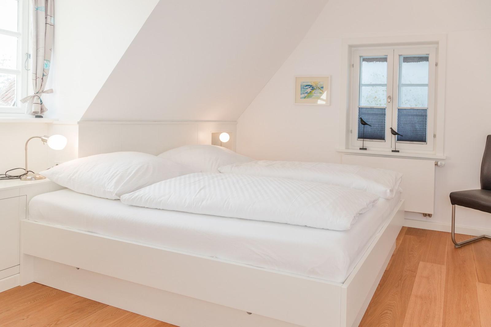 Ein Schlafzimmer mit Doppelbett, zwei Fenstern und Holzboden.