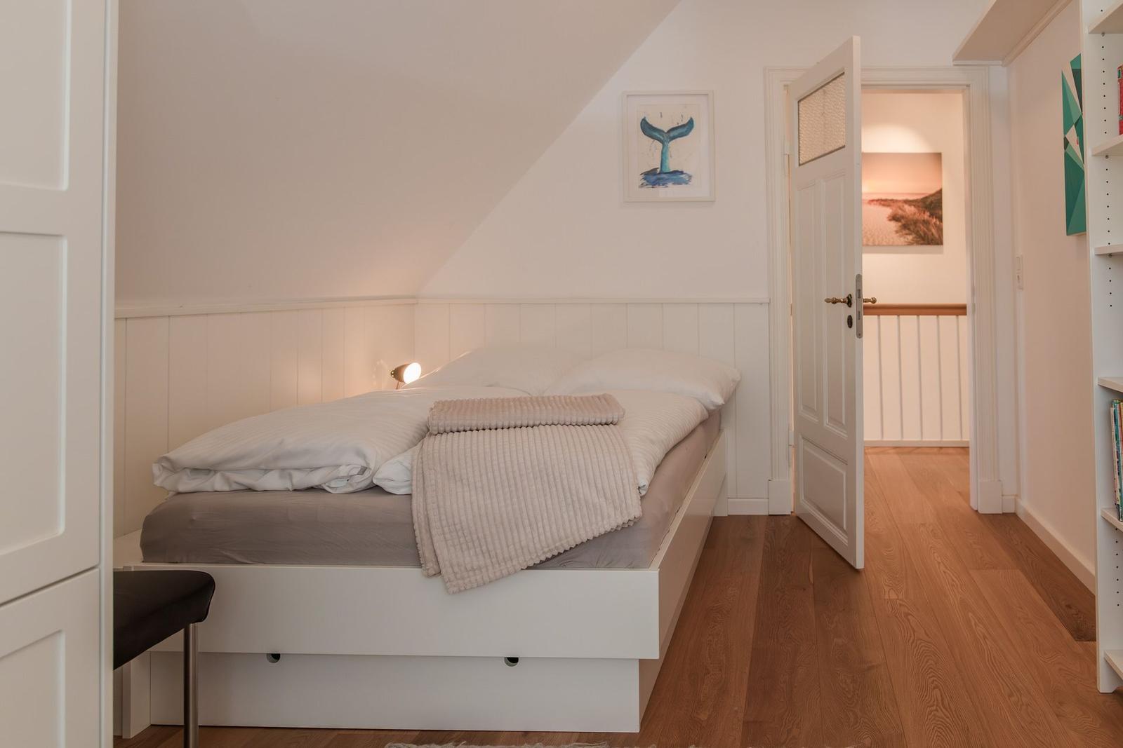 Schlafzimmer mit Bett, Wandbild und Holzboden. Tür führt in einen Flur.