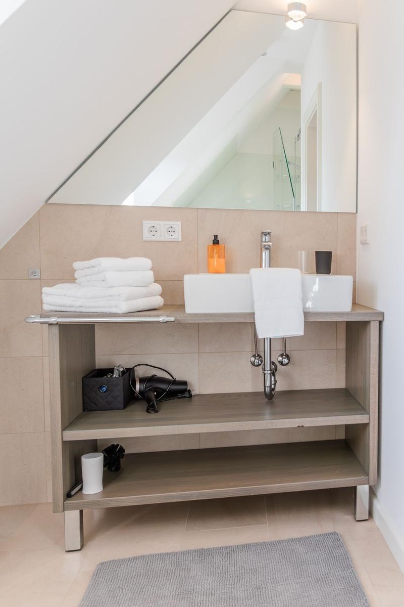 Badezimmer mit Waschbecken, Spiegel und Handtuchstapel unter Dachschräge.