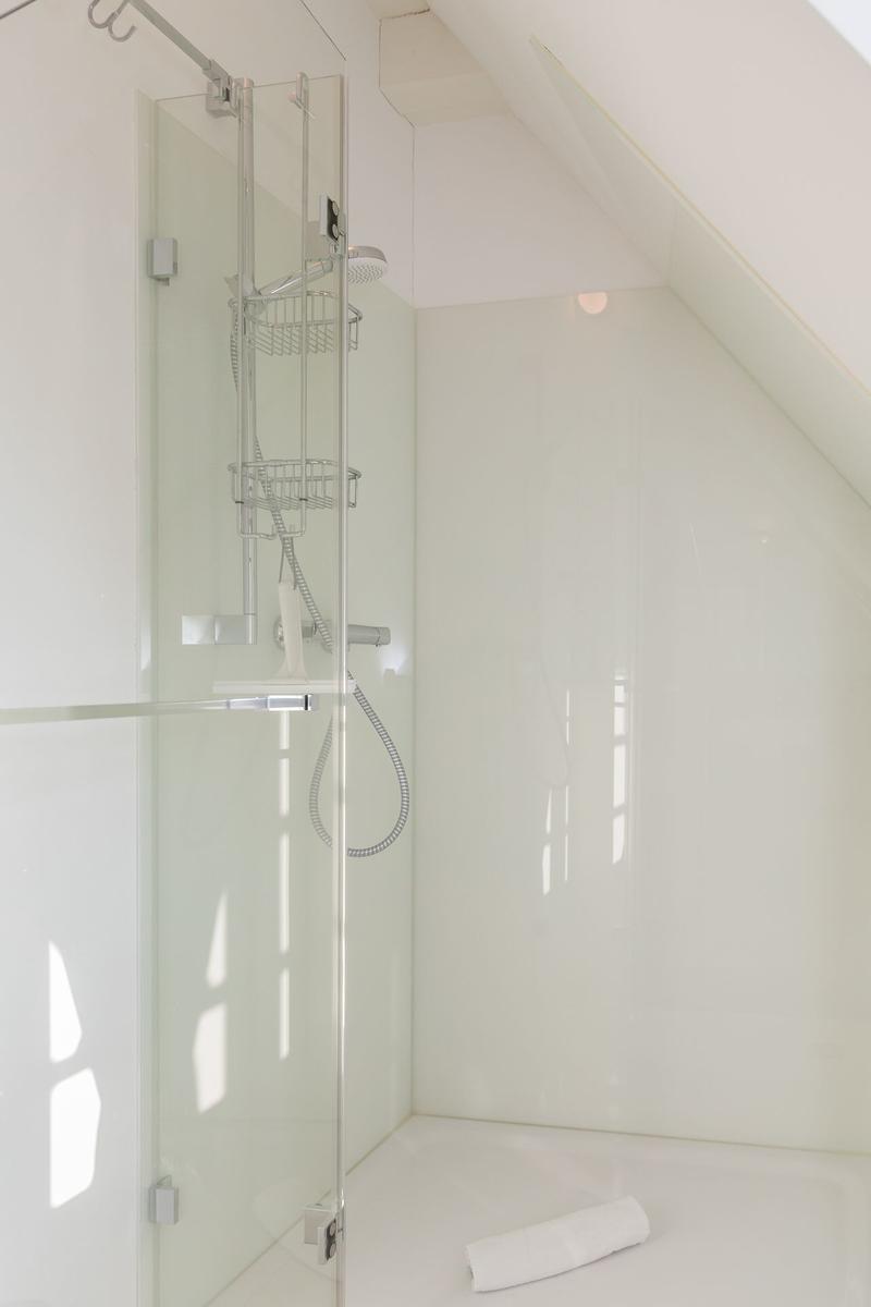 Dusche mit Glaswand, Duschbrause und Handbrause. Weiße Wände und Boden.