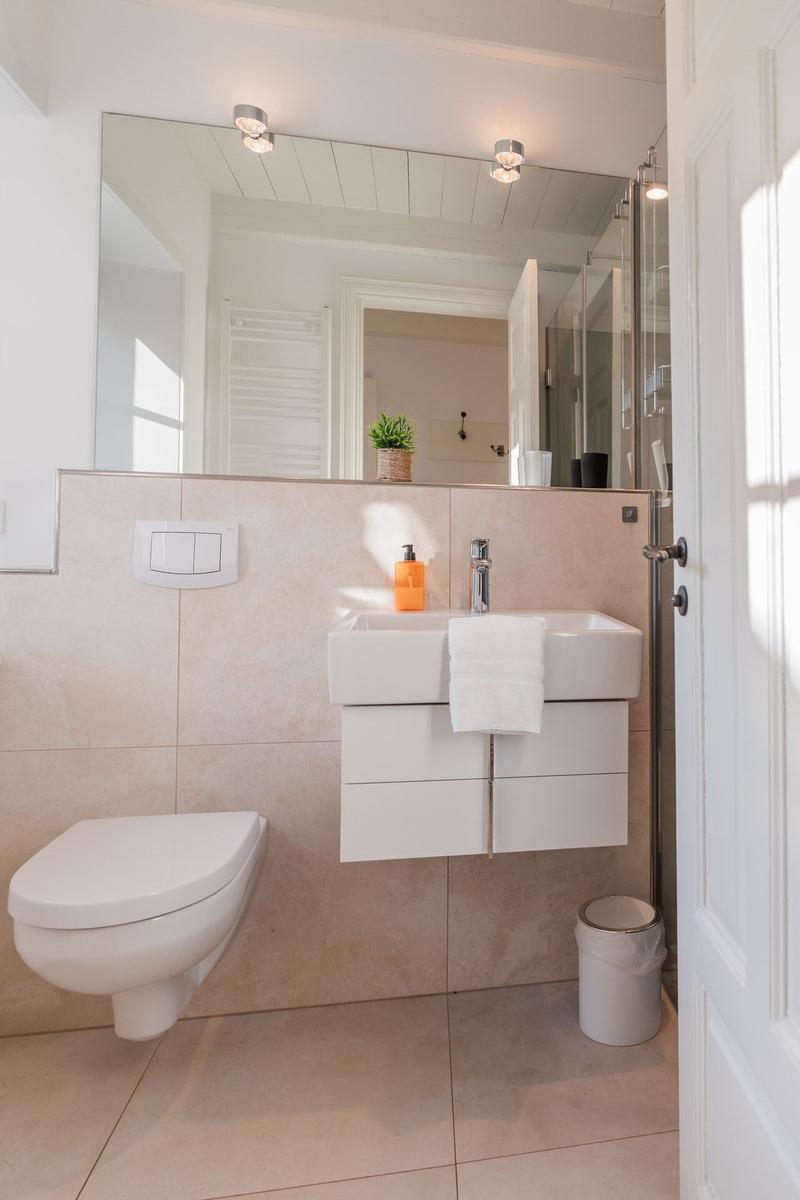 Badezimmer mit Waschbecken, Spiegel, Toilette und Dusche.