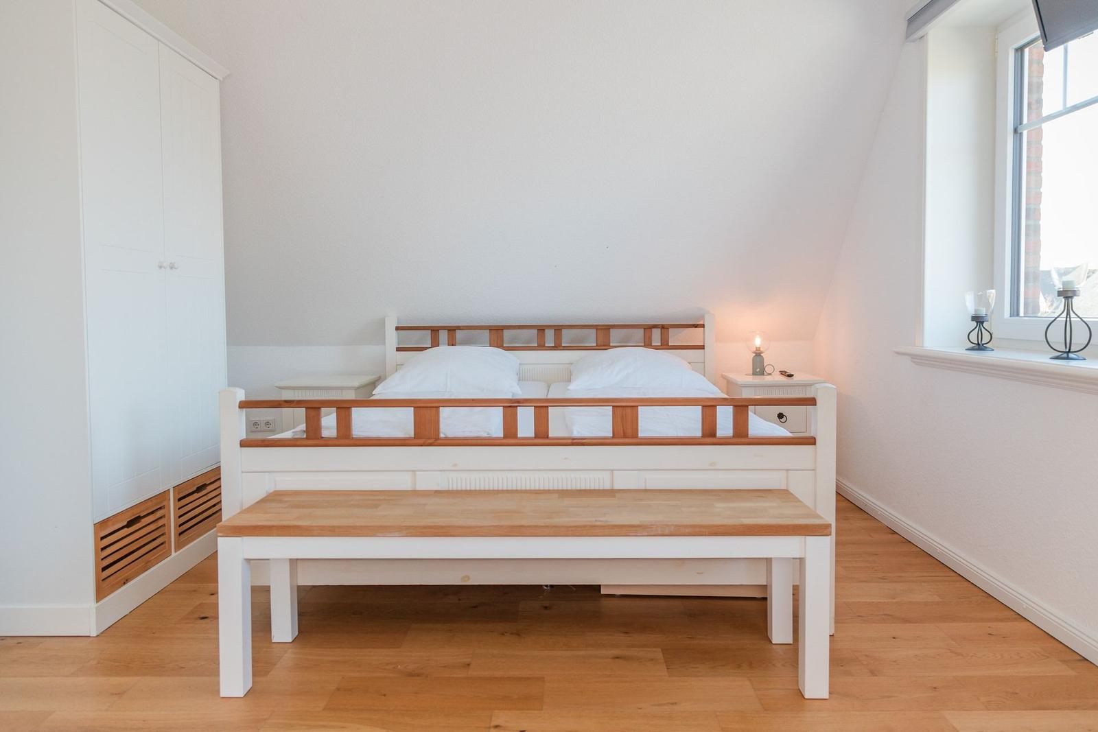 Schlafzimmer mit Doppelbett, Holzbank und Kleiderschrank. Fenster mit Blick nach draußen.