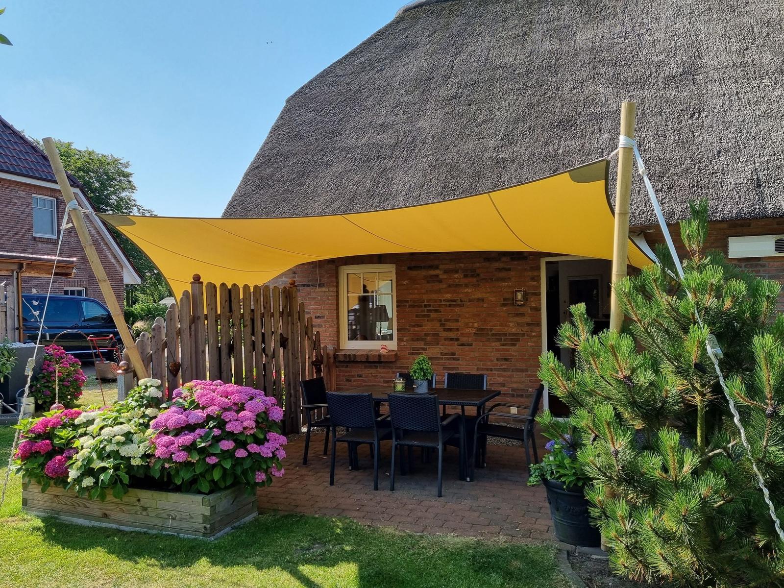 Terrasse mit Tisch, Stühlen und gelbem Sonnensegel unter strohgedecktem Dach.