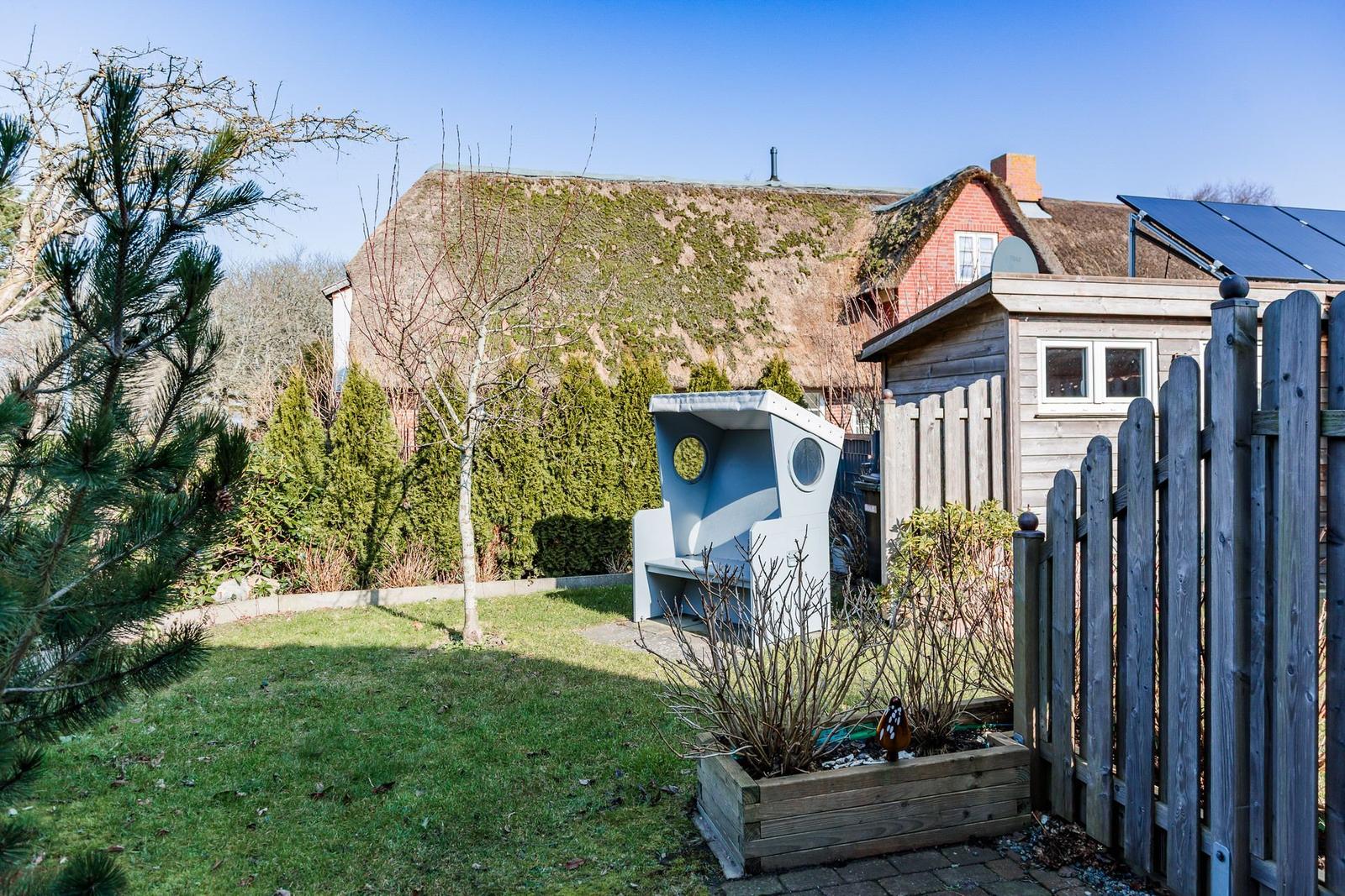 Hinterhof mit Garten, Holzzaun und einem hellblauen Sitzmöbel mit runden Öffnungen.
