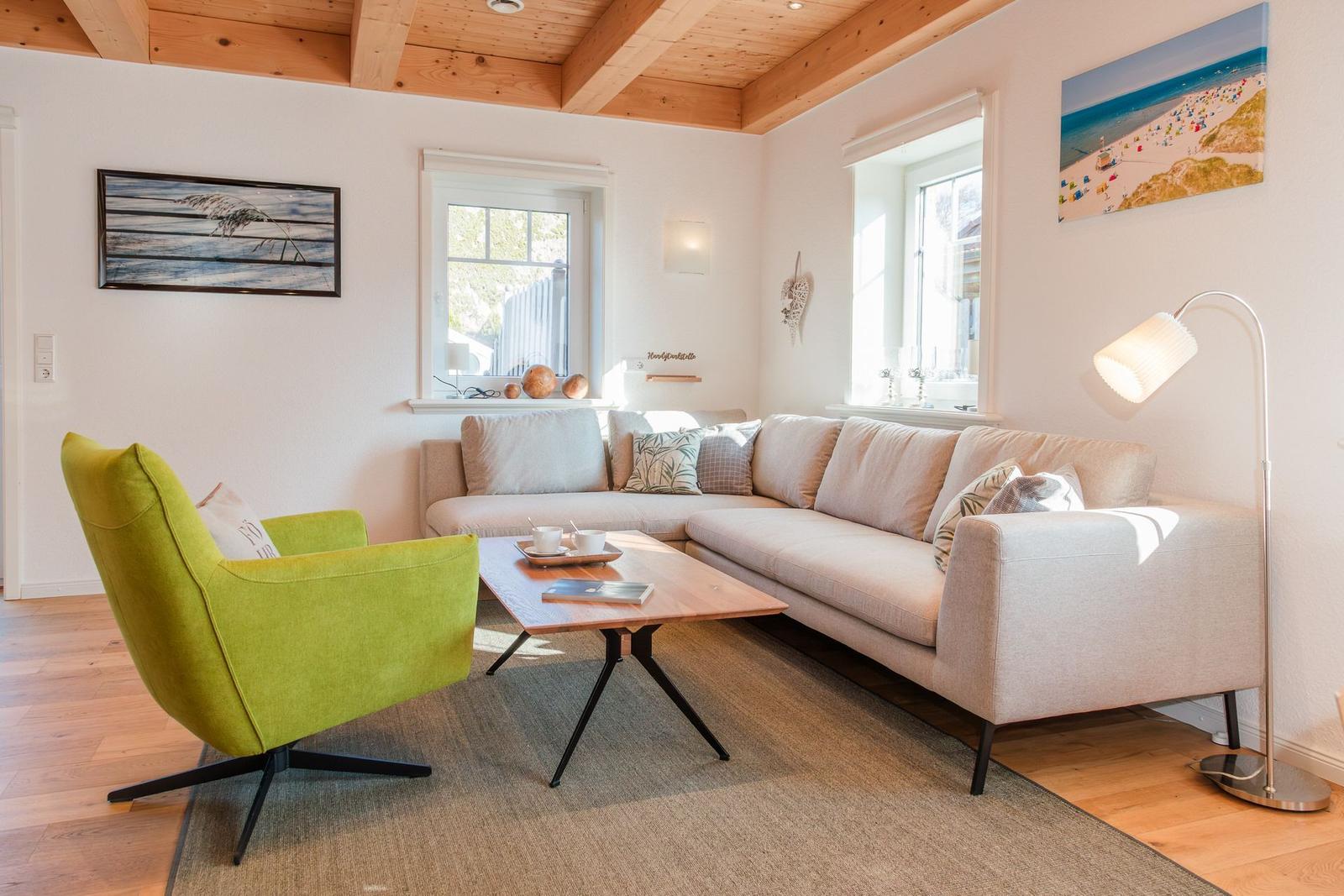 Wohnzimmer mit Sofa, grüner Sessel und Holztisch unter Holzbalkendecke.
