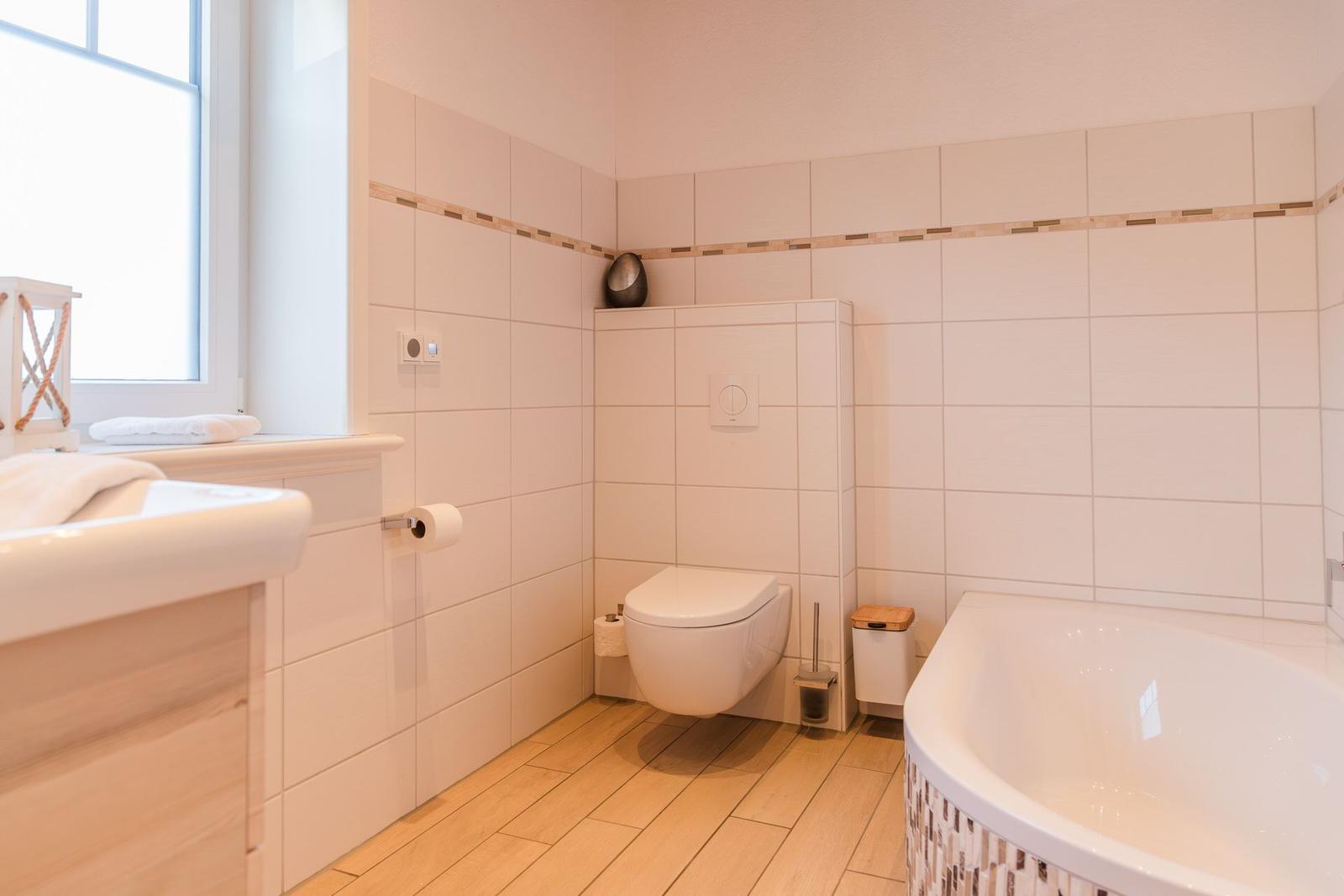 Badezimmer mit Badewanne, Toilette und Waschbecken. Fliesenwand und Holzboden.