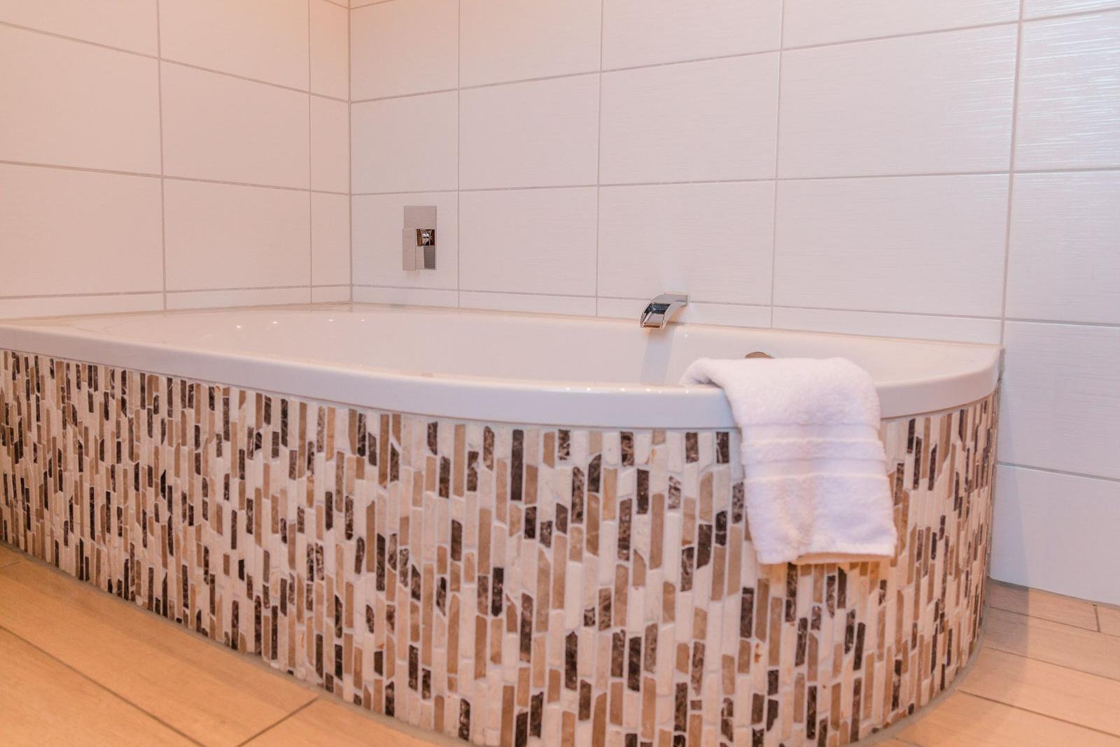 Badewanne mit Mosaikverkleidung und Handtuch