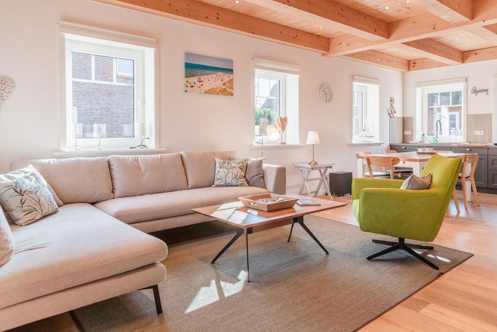 Wohnzimmer mit Sofa, grüner Sessel und Holzboden. Deckenbalken und Fenster sichtbar.