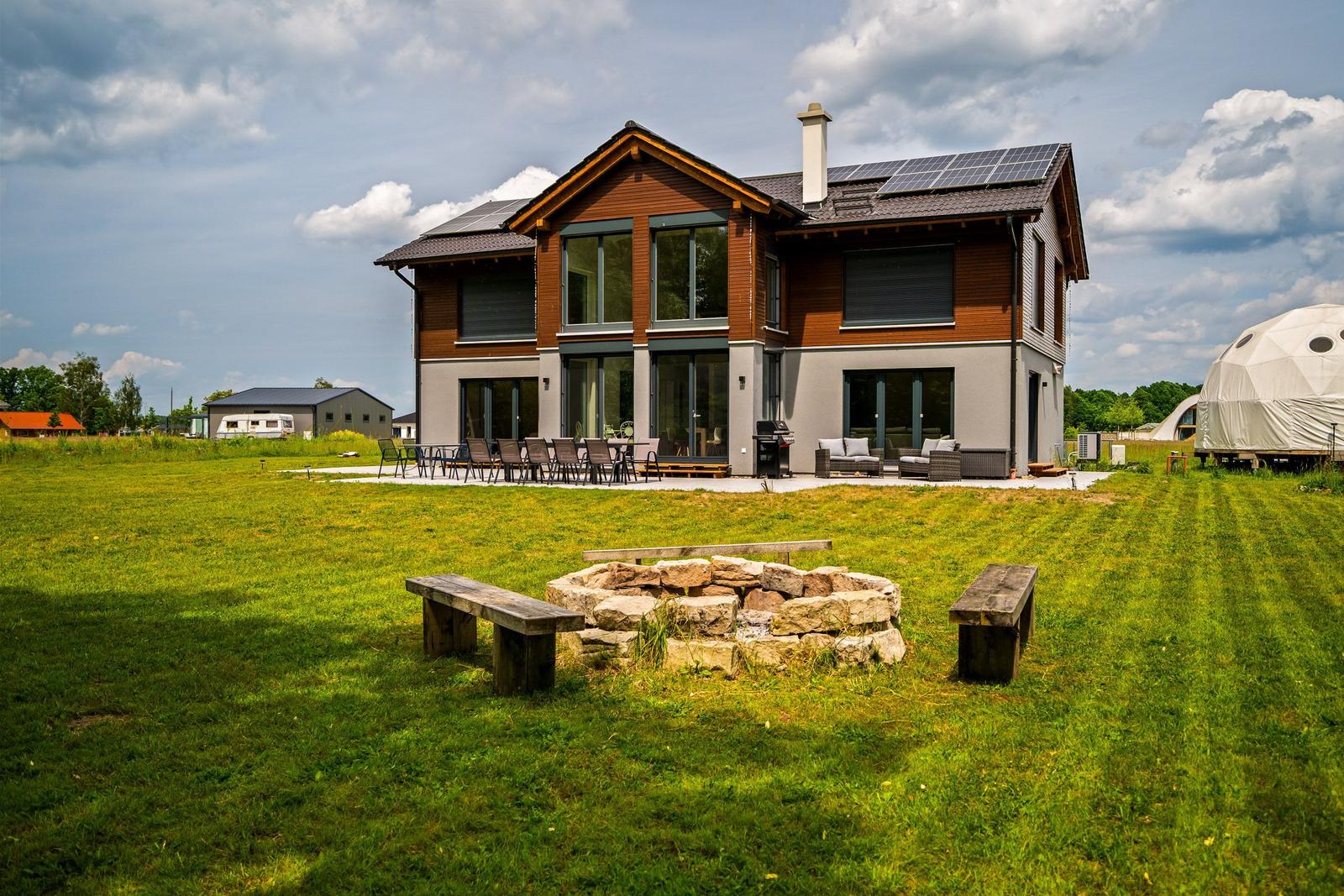 Moderne Villa mit Terrasse, Grill und Steinfeuerplatz auf grünem Grundstück.