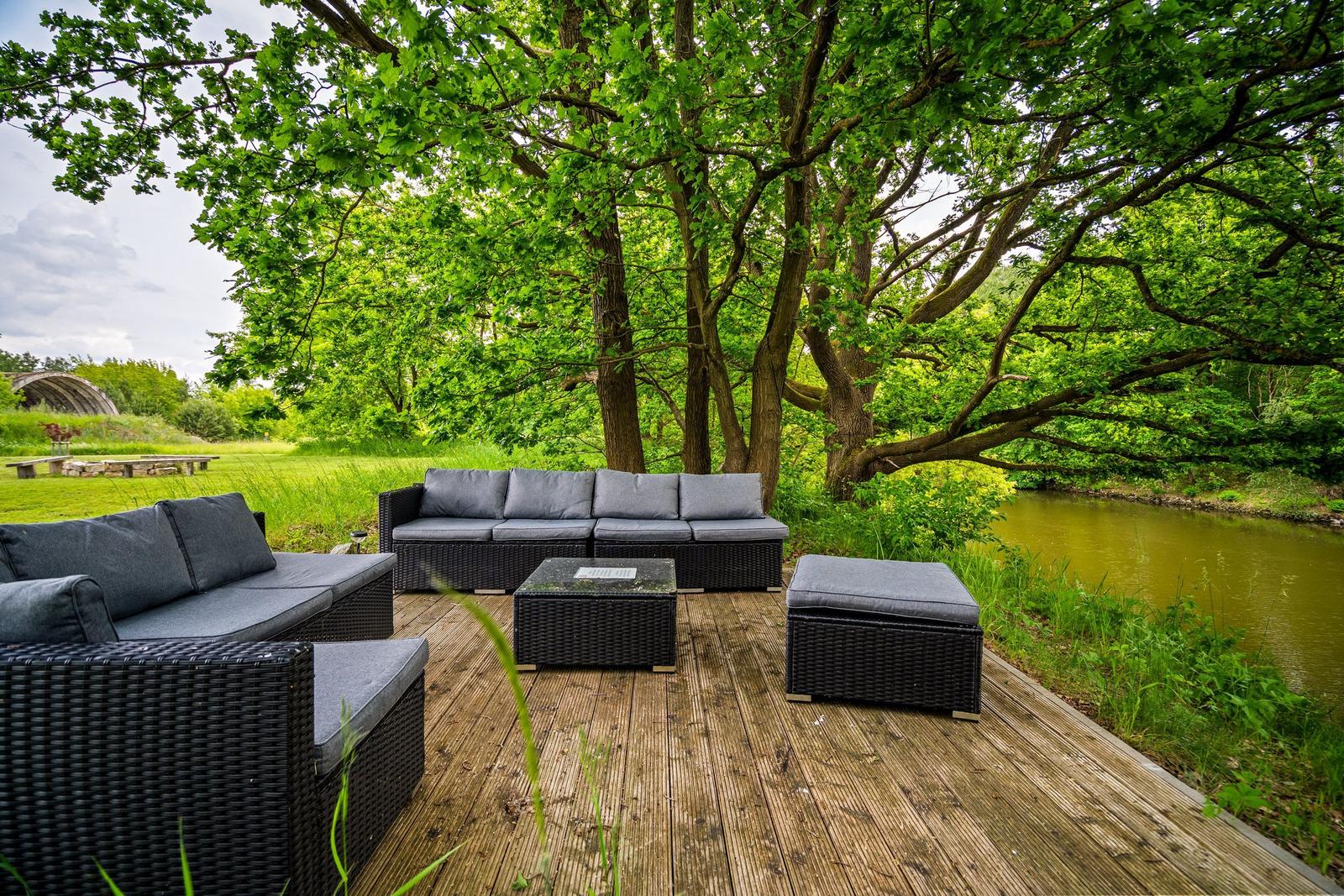Terrasse mit Sitzgruppe unter Bäumen am Fluss