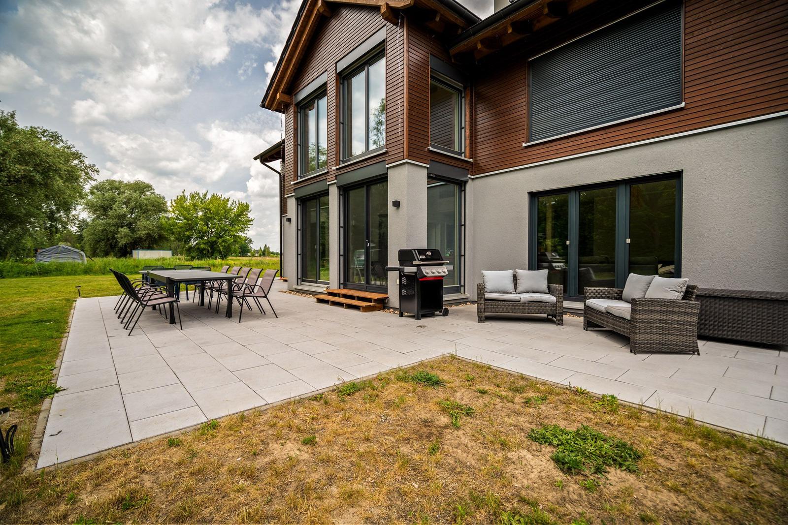 Terrasse mit Grill, Sitzgruppe und Tisch. Modernes Haus mit großem Außenbereich.