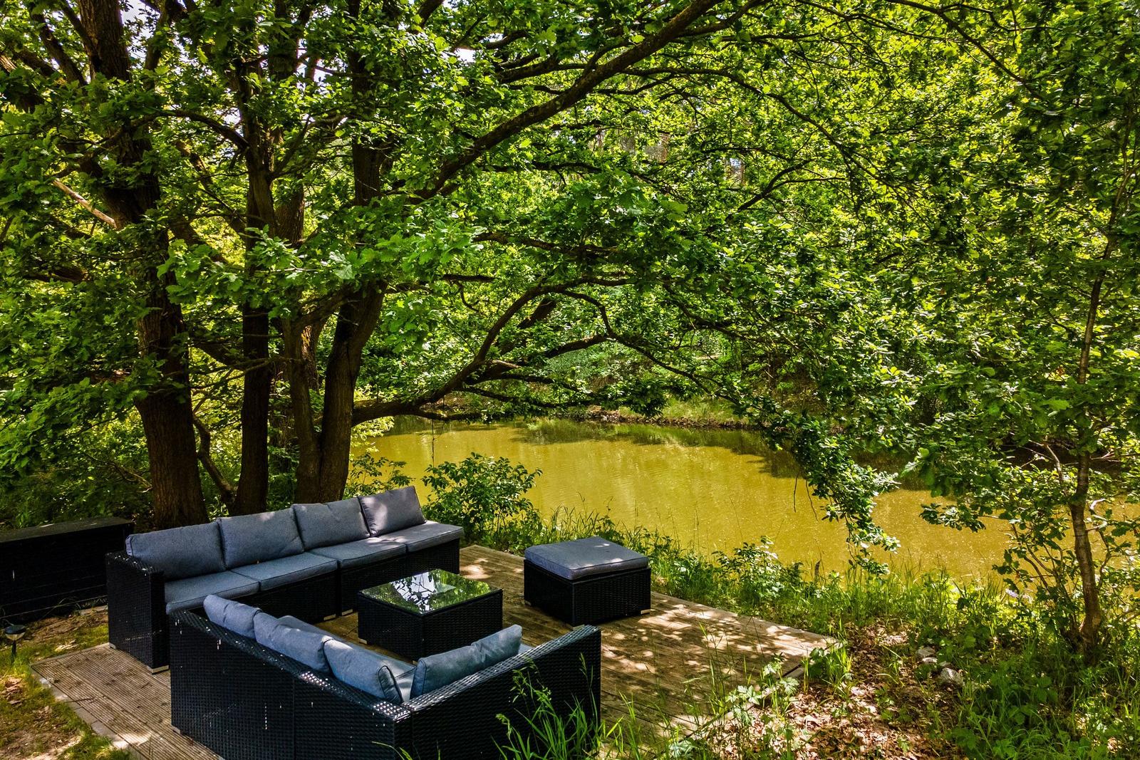 Terrasse mit Sitzgruppe unter Bäumen am Teich